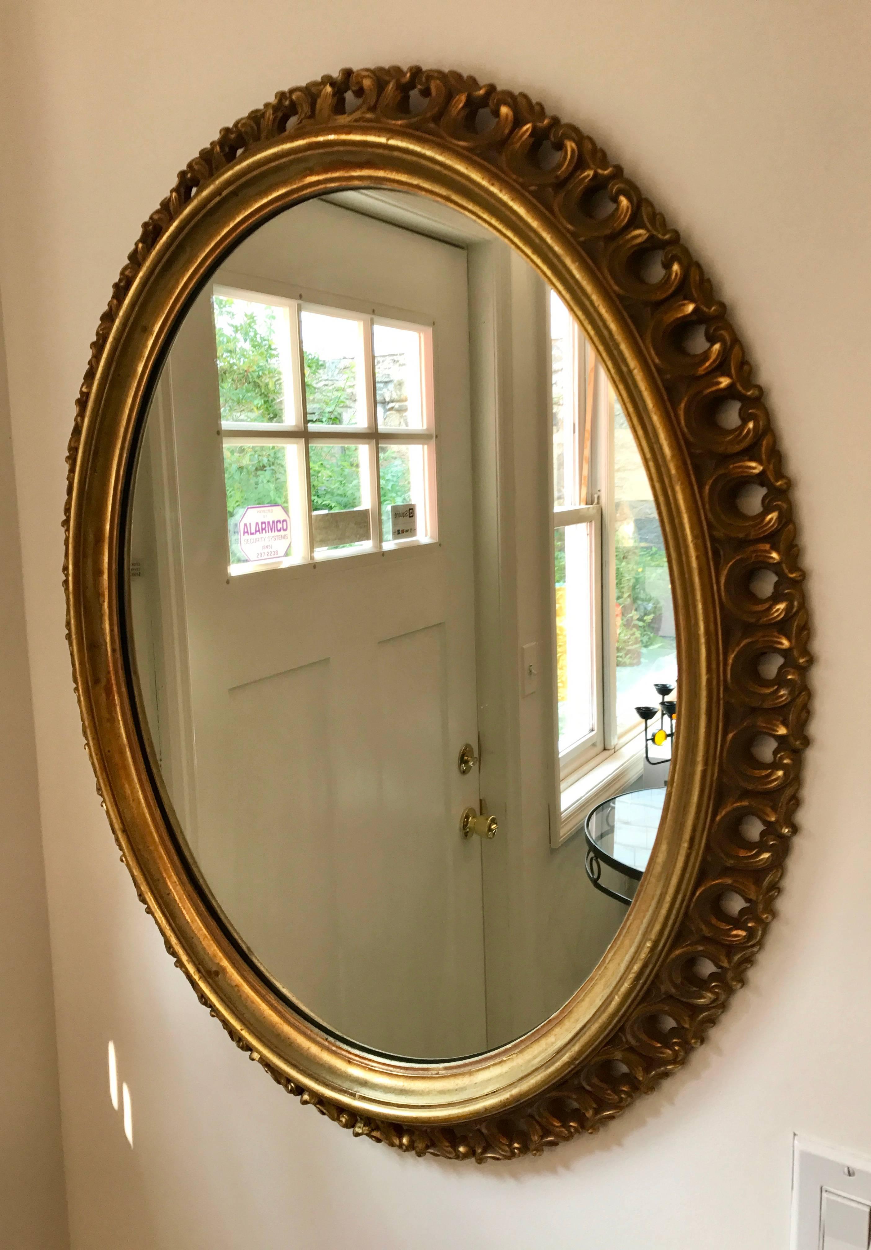 Beautiful large oval wall mirror. Lovely aged gold patina. Simple and elegant scrollwork around perimeter. Perfect for either Mid-Century, Hollywood Regency, or Traditional decor.