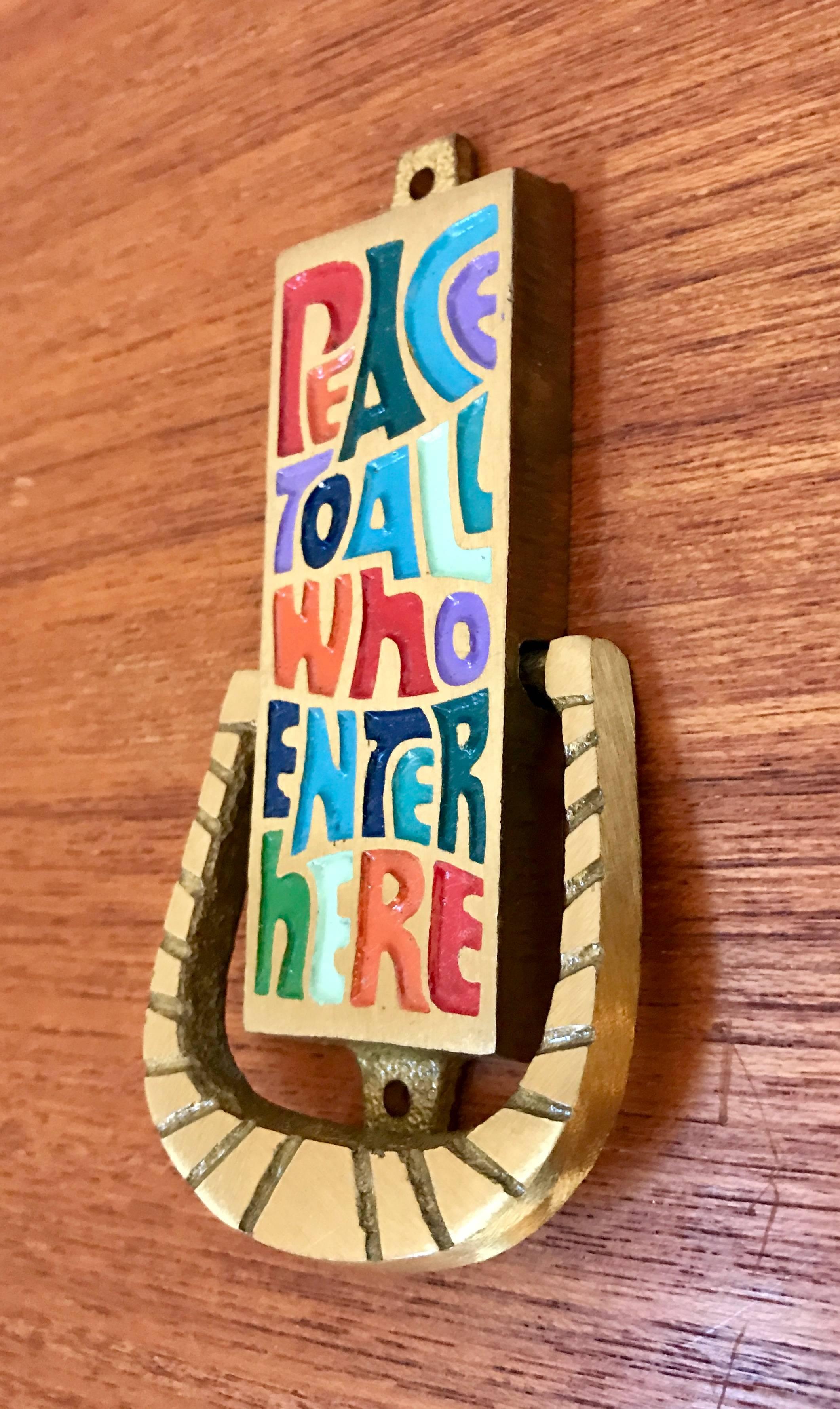 Very cool small midcentury door knocker titled "peace to all who enter here"  made of brass with colorful enameled lettering.  Manufactured by Terra Sancta Guild, Isreal, 1969