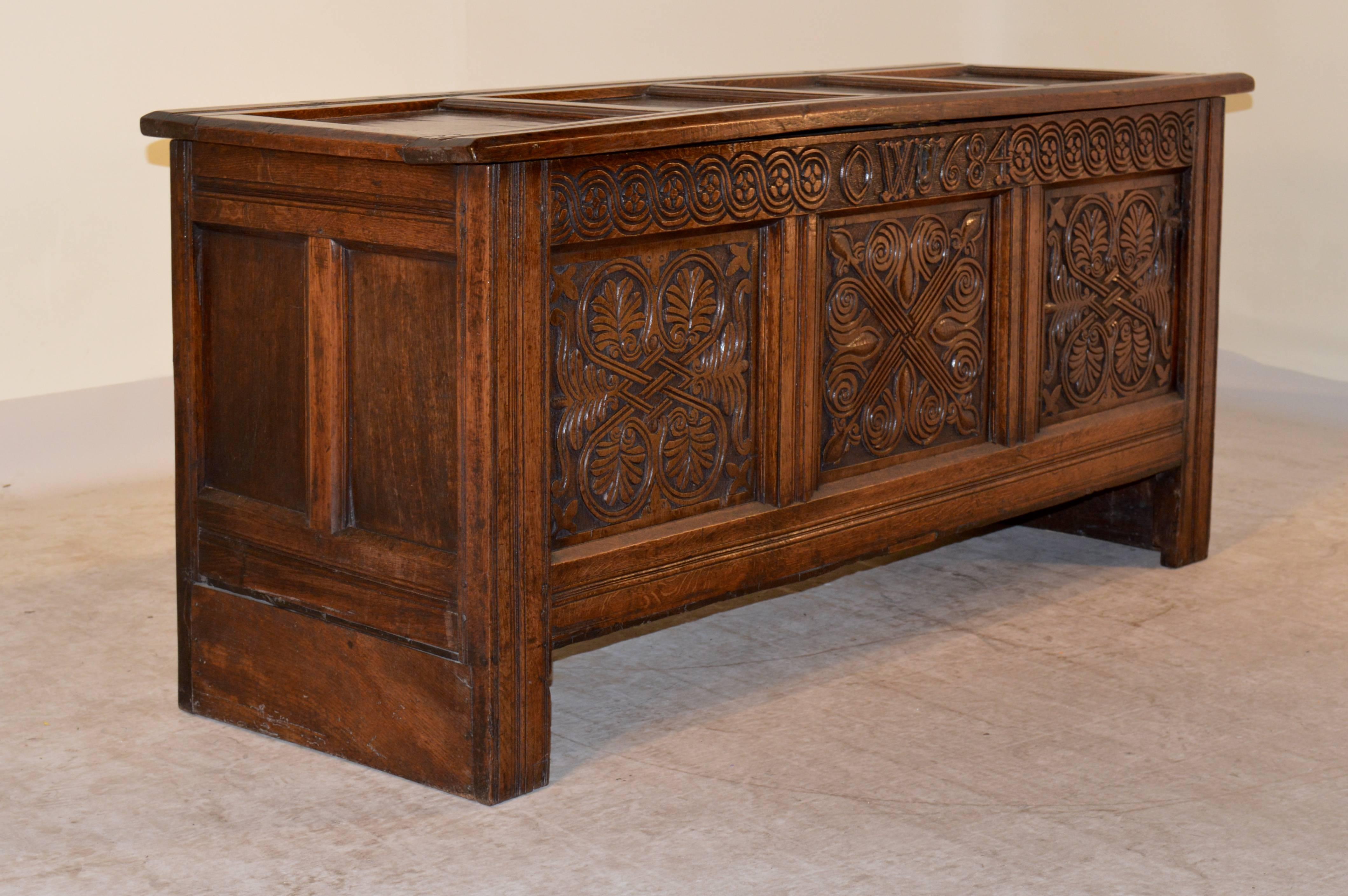 17th century English oak blanket chest with a paneled top and sides. The front has carved decoration and has a hand-carved date of 1684 and the initials OW. The hinges and lock have been replaced.