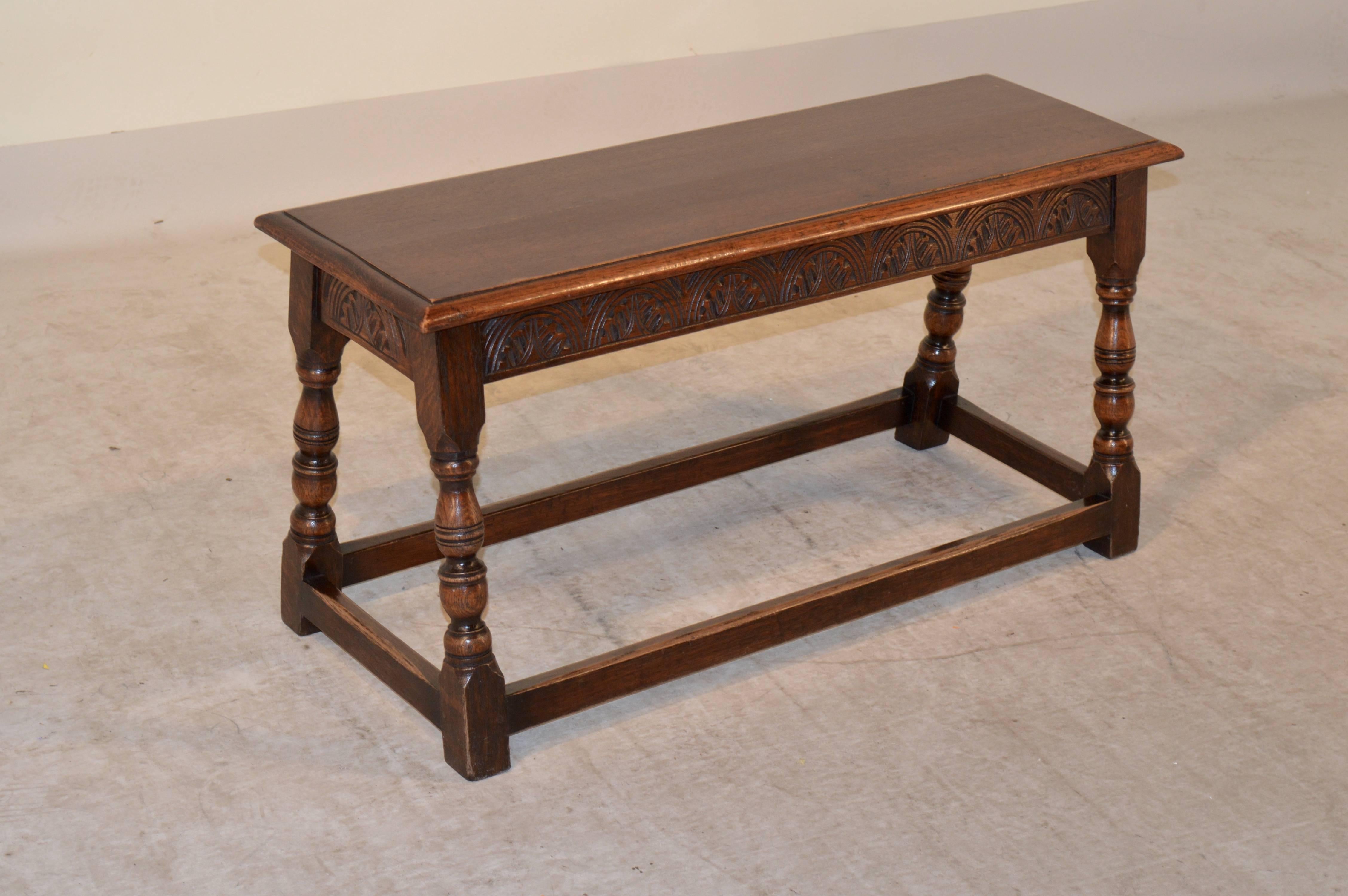 Late 19th century English oak joint bench with a beveled edge around the top following down to a carved decorated apron and hand-turned splayed legs, which are joined by stretchers.