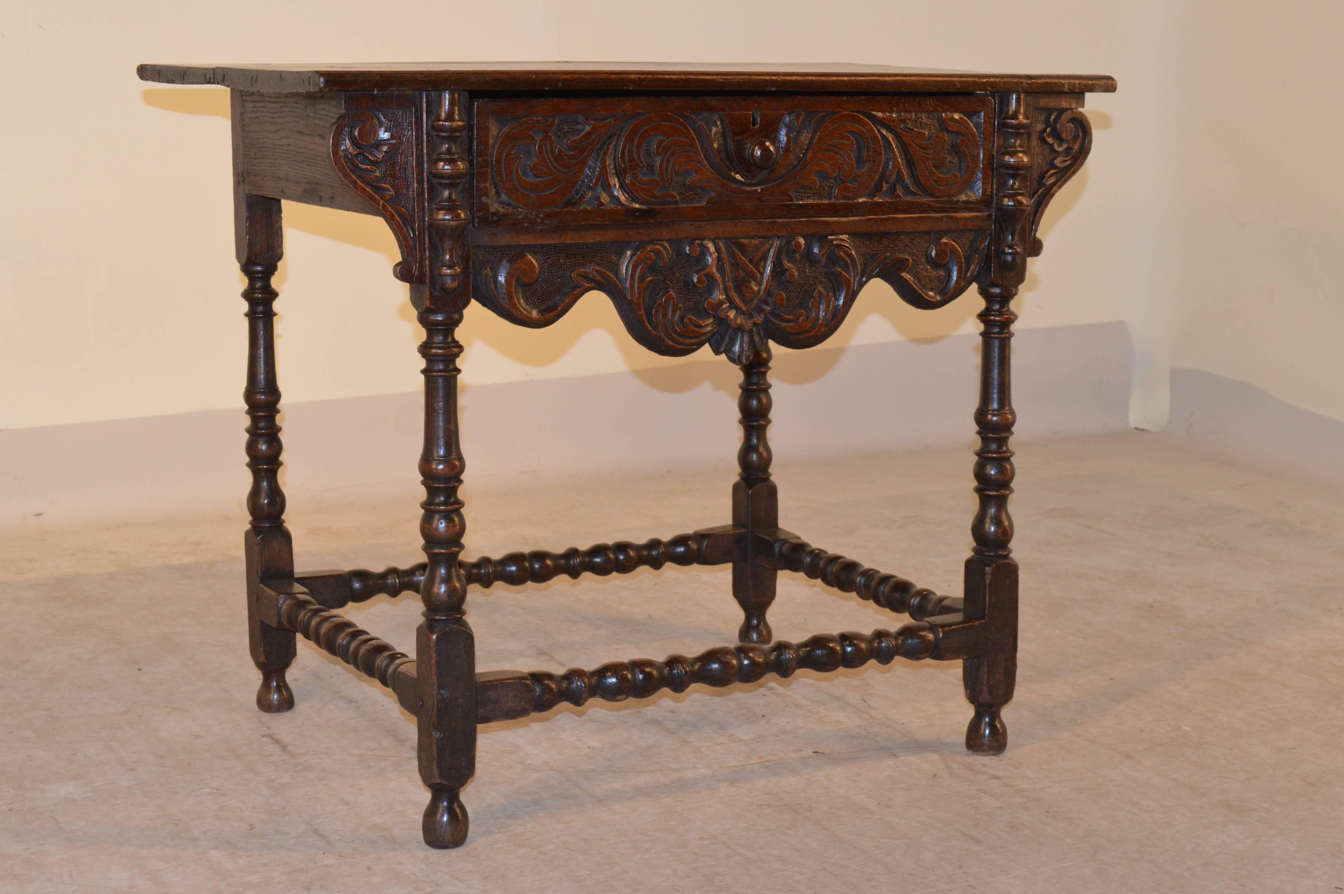 18th century English oak side table with a two plank top, which has a routed edge. The apron is simple on the sides and contains a single drawer with a carved decorated drawer front, flanked by applied turnings and carved brackets and a scalloped