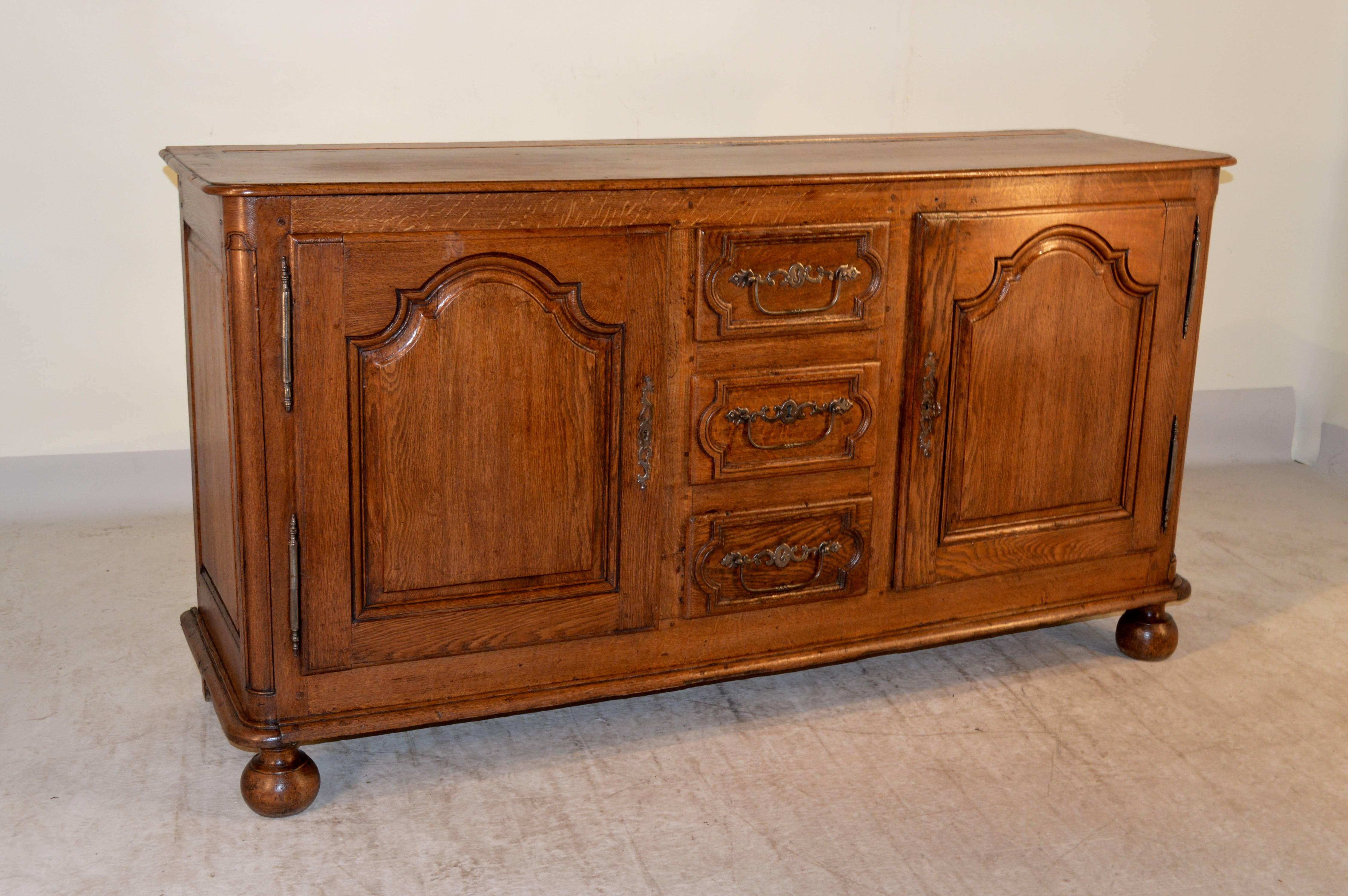 18th century French enfilade made from oak with a beveled edge around the top, which also has a plate rail. The case has paneled sides and two doors with raised panels flanking three central drawers, which have raised paneled drawer fronts and
