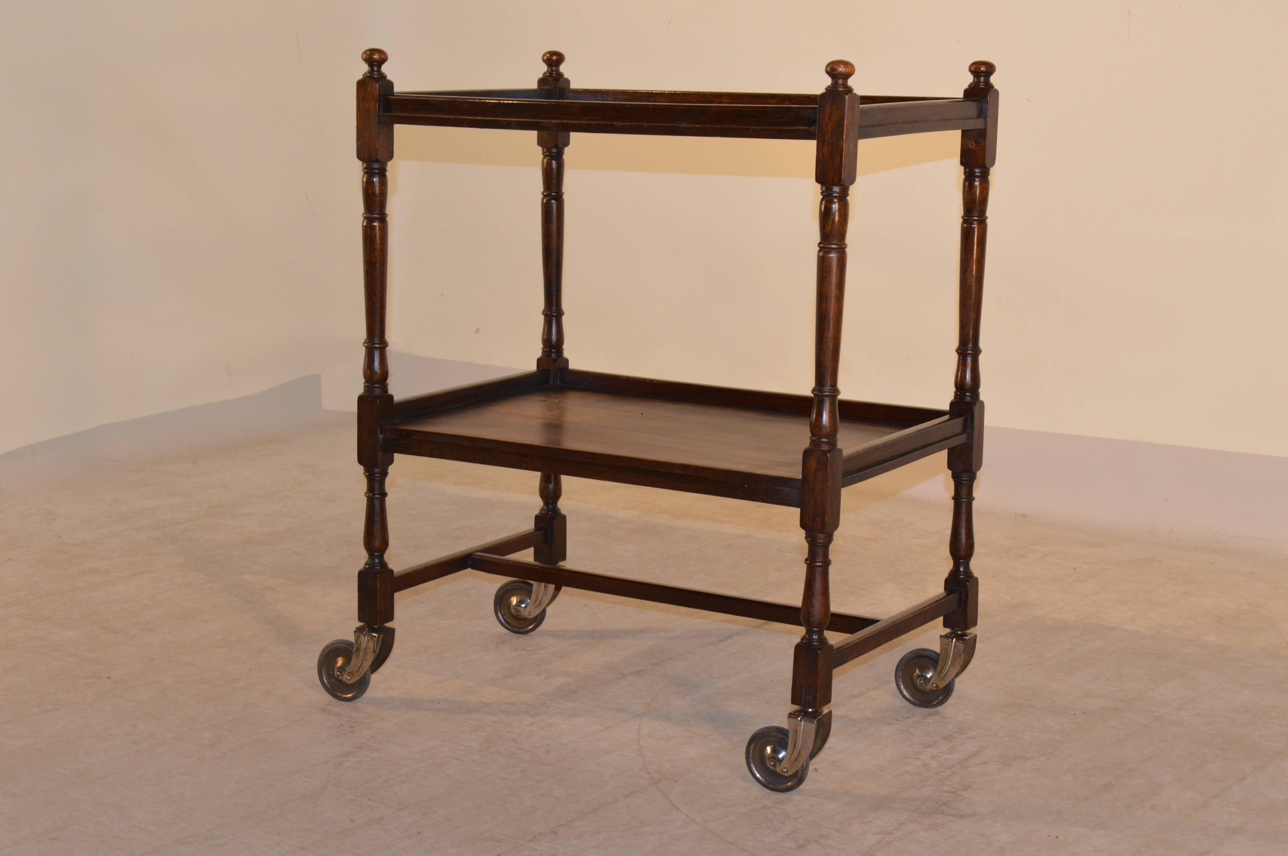 English oak drinks cart with two shelves, hand-turned legs joined by a cross stretcher and raised on casters, circa 1900.