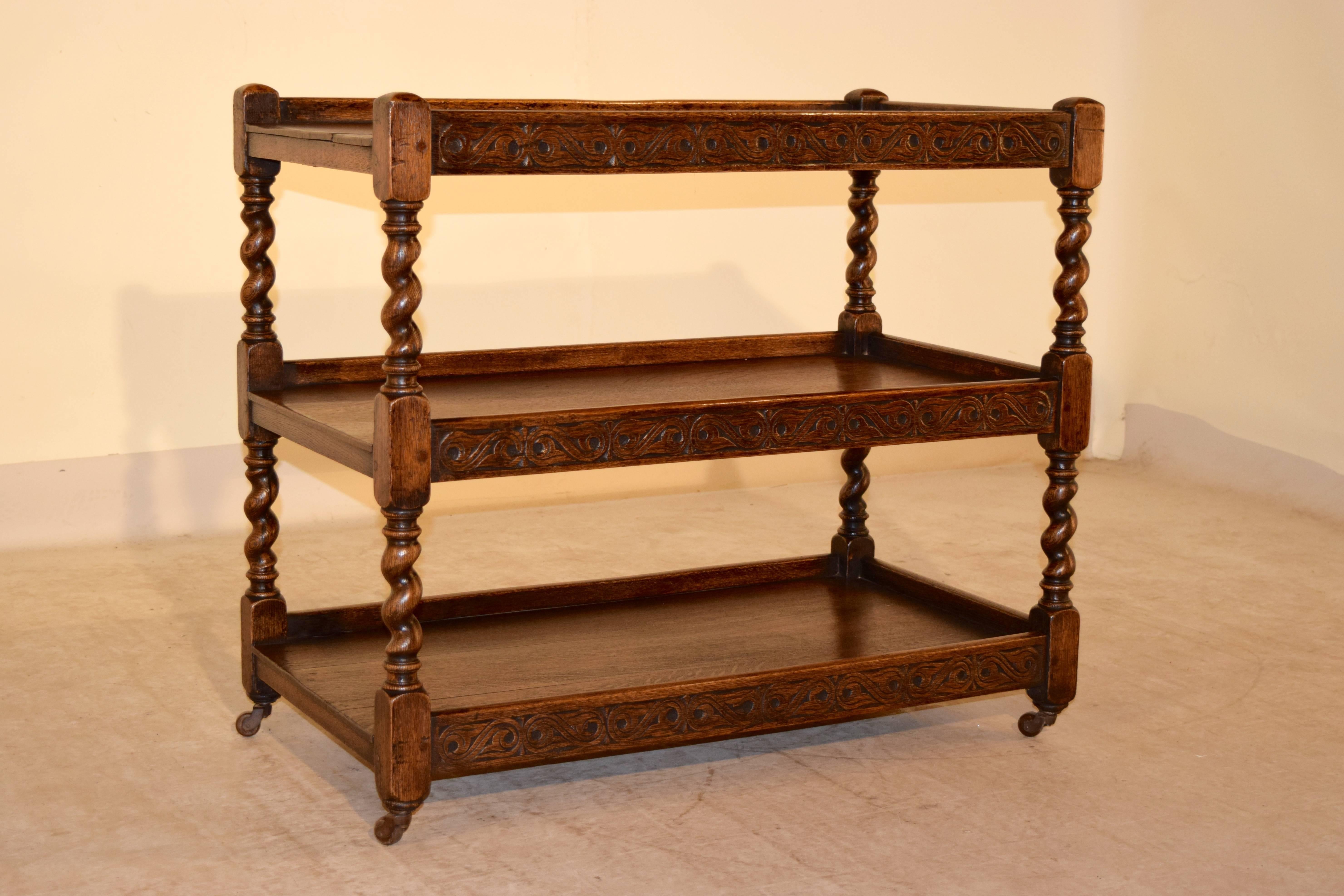 19th century English oak drinks cart in an unusually large size. The piece has three shelves separated by hand turned barley twist shelf supports and ending in original casters. The galleries have hand-carved designs as well.