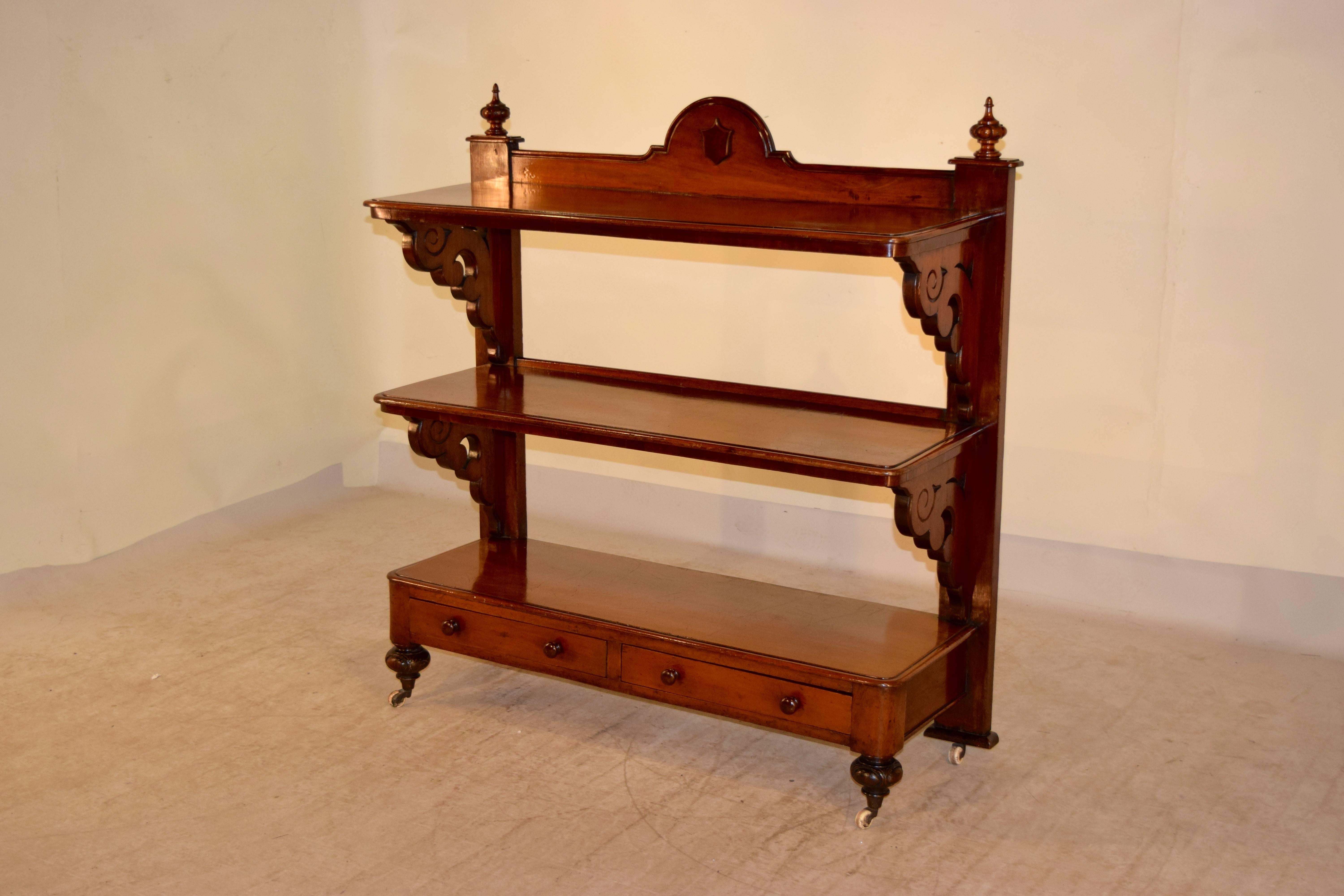 19th century English buffet made from mahogany. The top has a lovely arch and is decorated with a central shield embellishment, also made from mahogany. This piece has three shelves, which have hand-carved and decorated shelf supports. The bottom