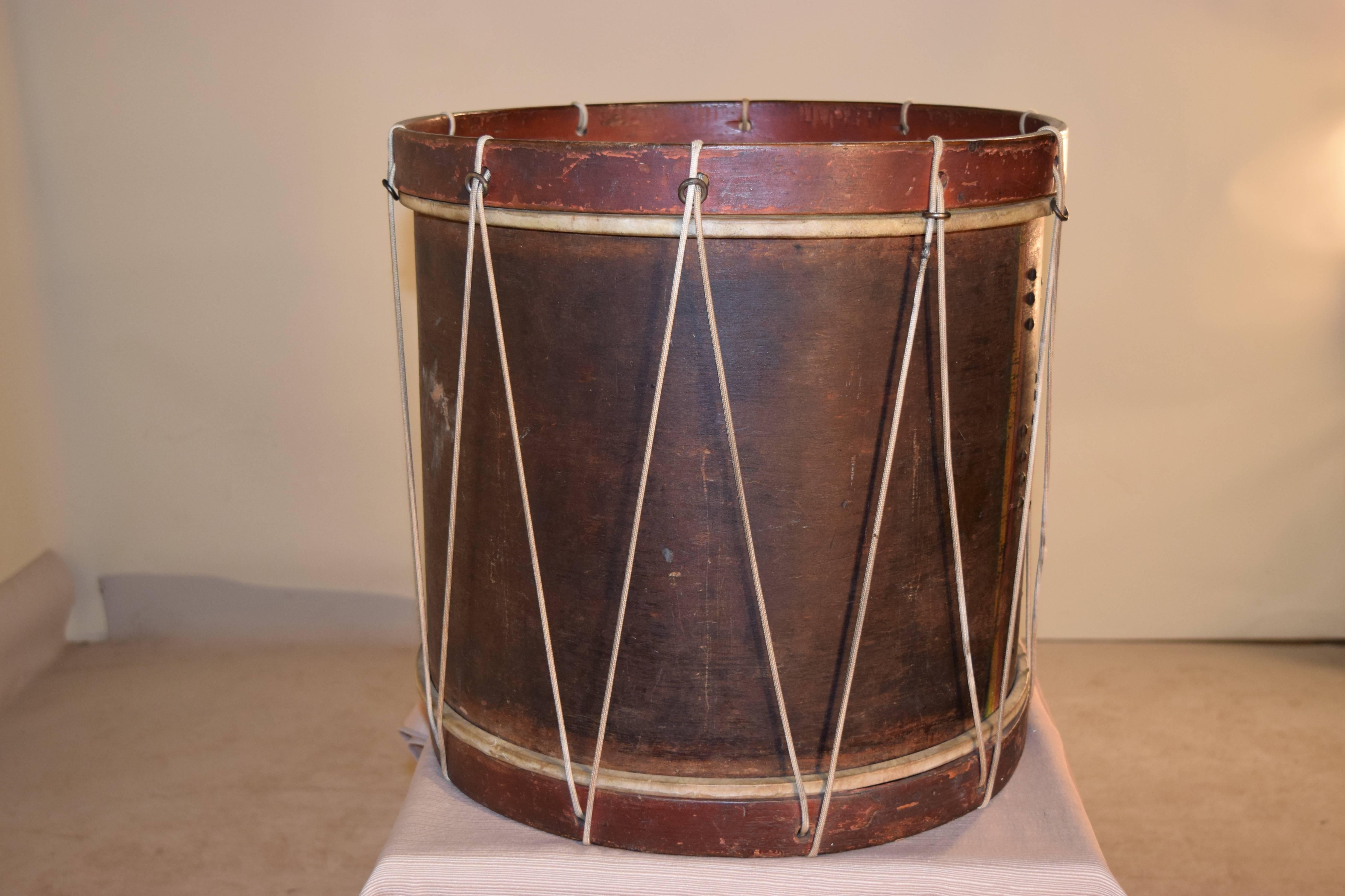 19th century American rope tension military snare drum. It is paint decorated with wooden hoops and a red painted background with red and yellow lines framing a central tulip and sunburst decoration. The rope has been modernized. It has calfskin