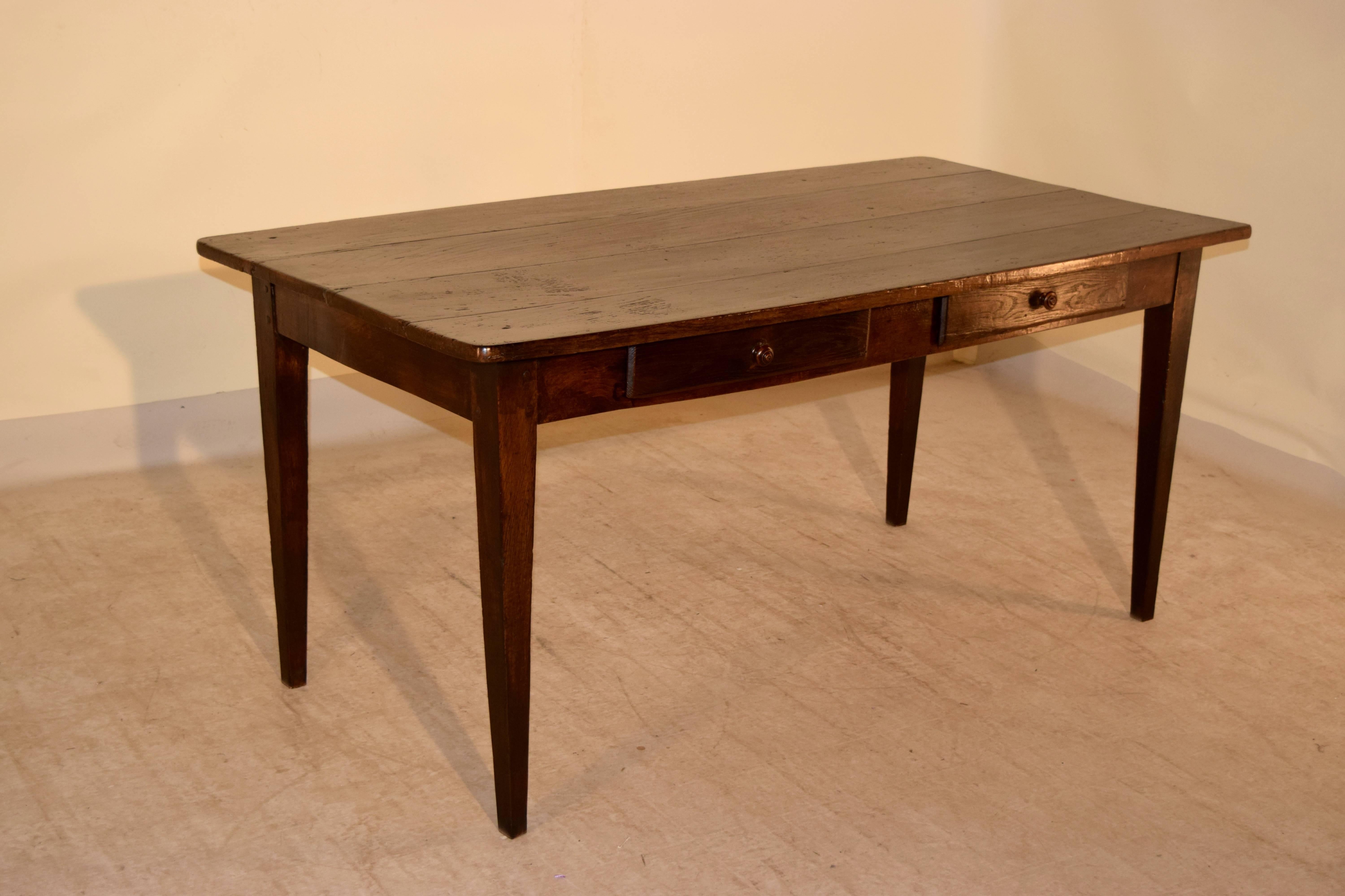 Early 19th century French farm table made from Chestnut. It has a four plank top and a simple apron with two drawers following down to simple tapered legs. The apron measures 24.88