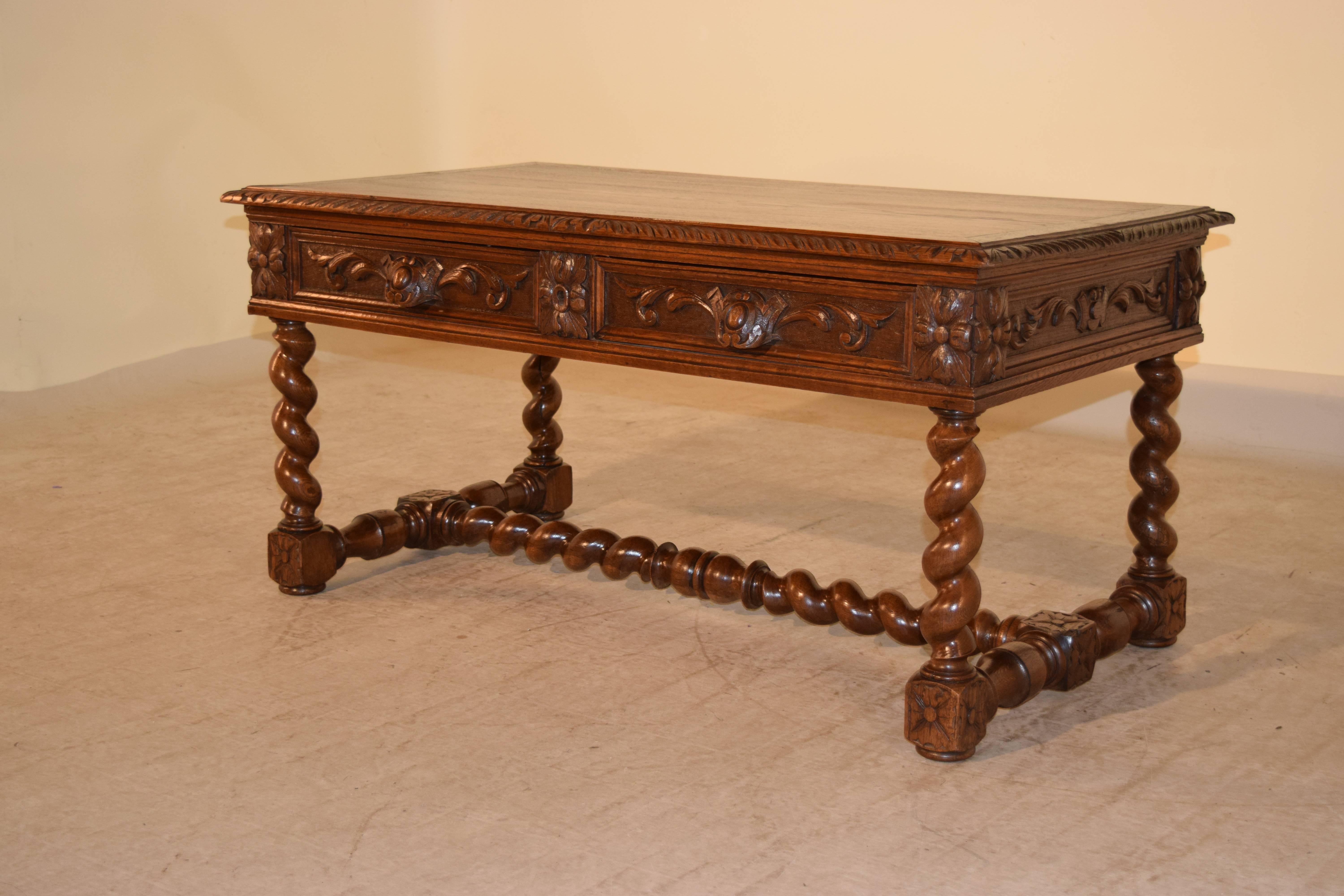 19th century French coffee table made from oak. The top is banded and has a beveled and gadrooned edge, following down to a carved decorated apron with two drawers on the front and supported on hand-turned barley twist legs, joined by barley twist