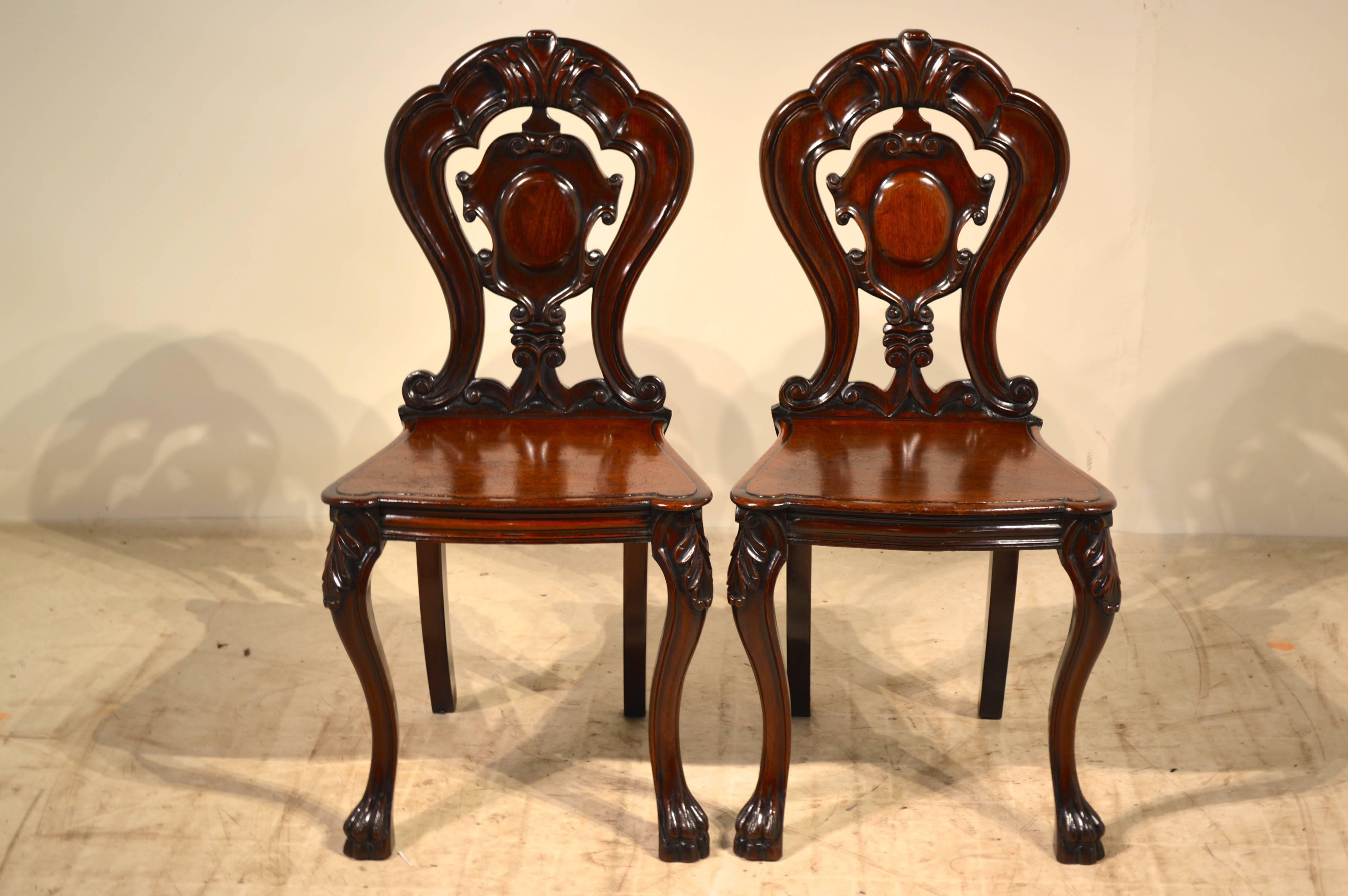 19th century pair of English mahogany hall chairs with wonderfully carved and pierced vase backs, scalloped and beveled front edges on the seats, and lovely splayed legs in the back and cabriole legs in the front ending in carved paw feet. Seat