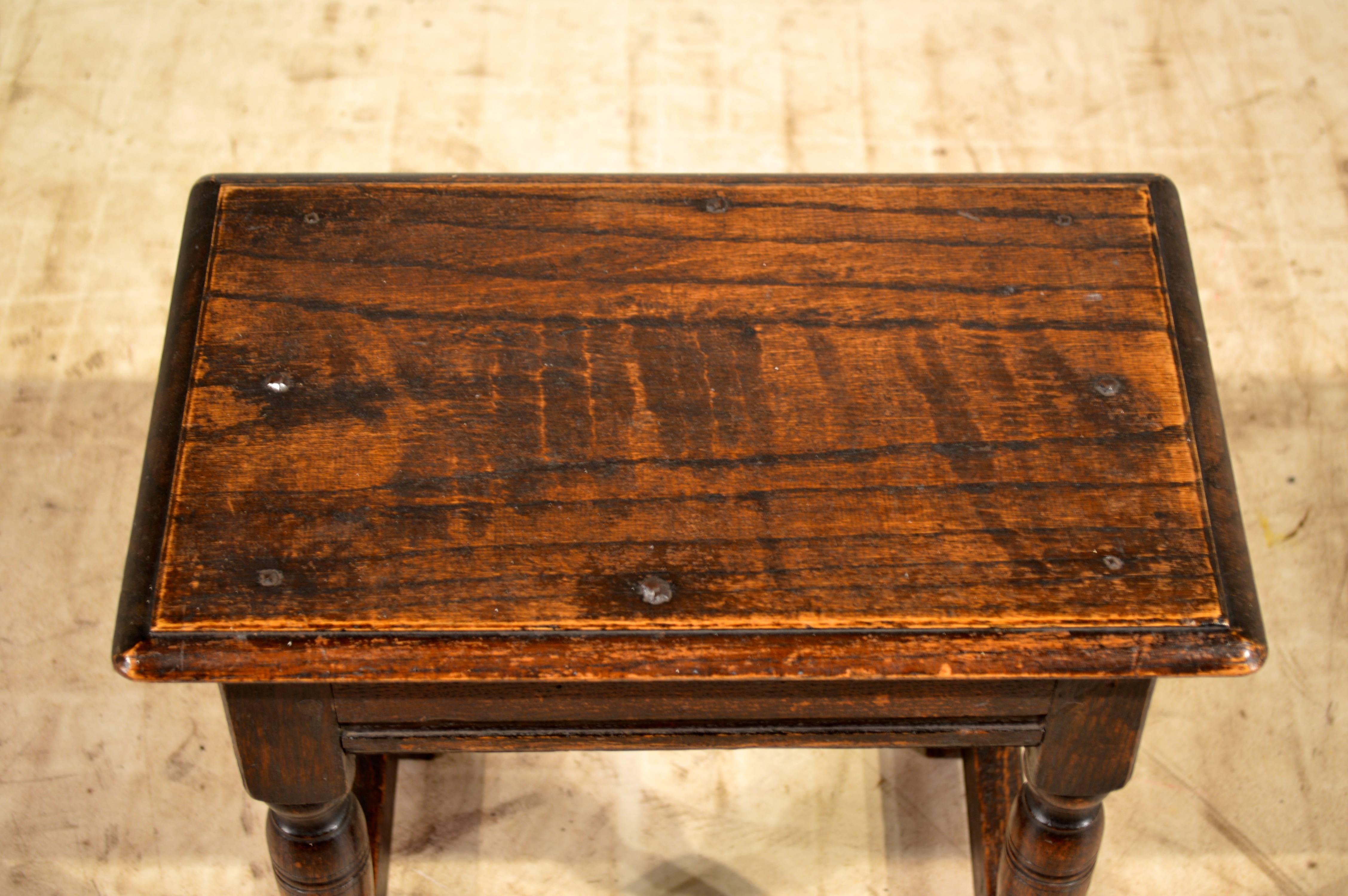 19th century English joint stool made from oak. The top is beveled around the edge and retains the original rose head nail construction. The apron is simple and has a routed edge and lovely turned legs joined by thick stretchers.