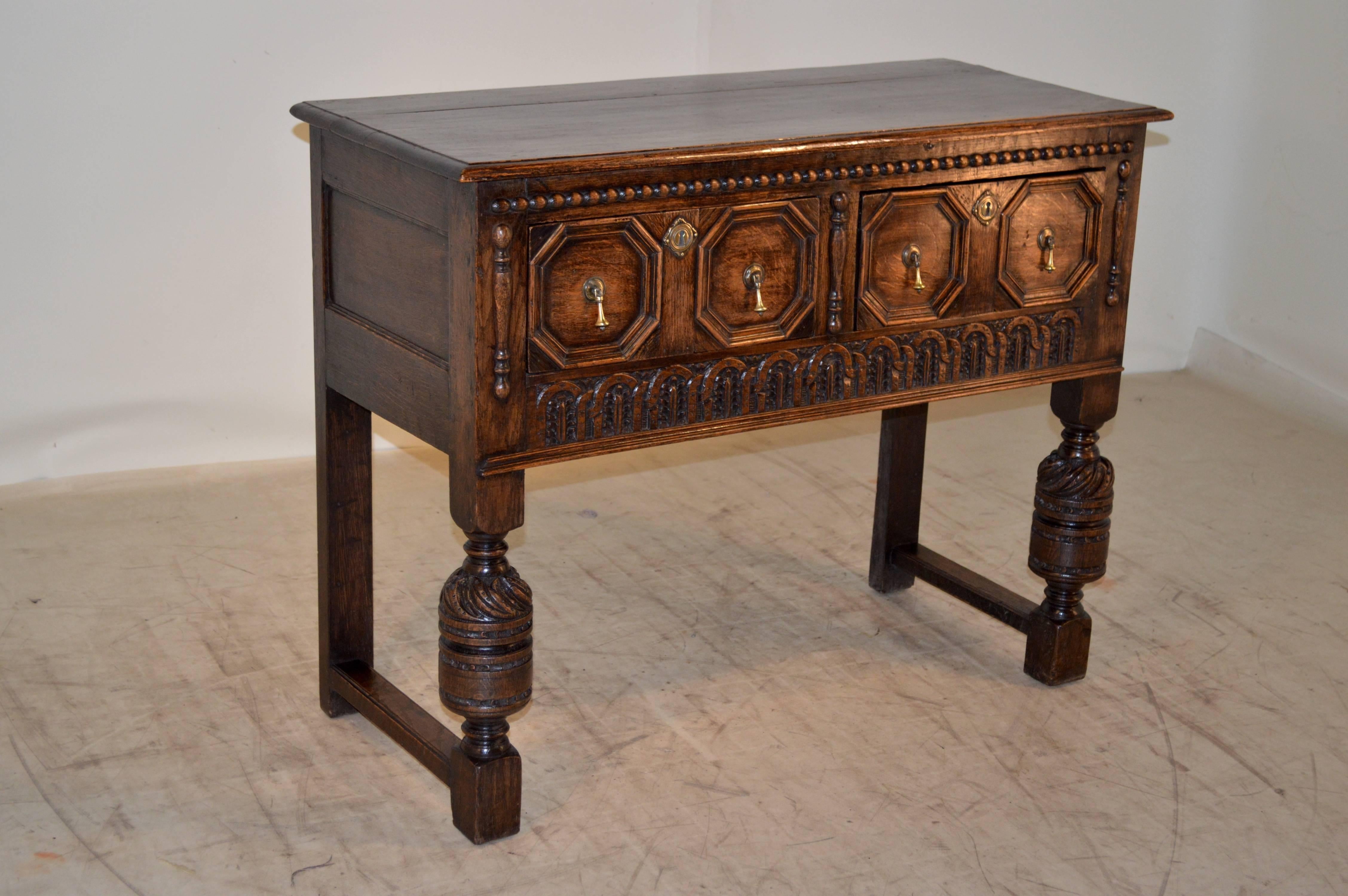 19th century English oak small server with a beveled edge around the top following down to paneled sides and two drawers on the front of the piece which have geometric raised panels. They are flanked with applied turnings, beaded molding, and a
