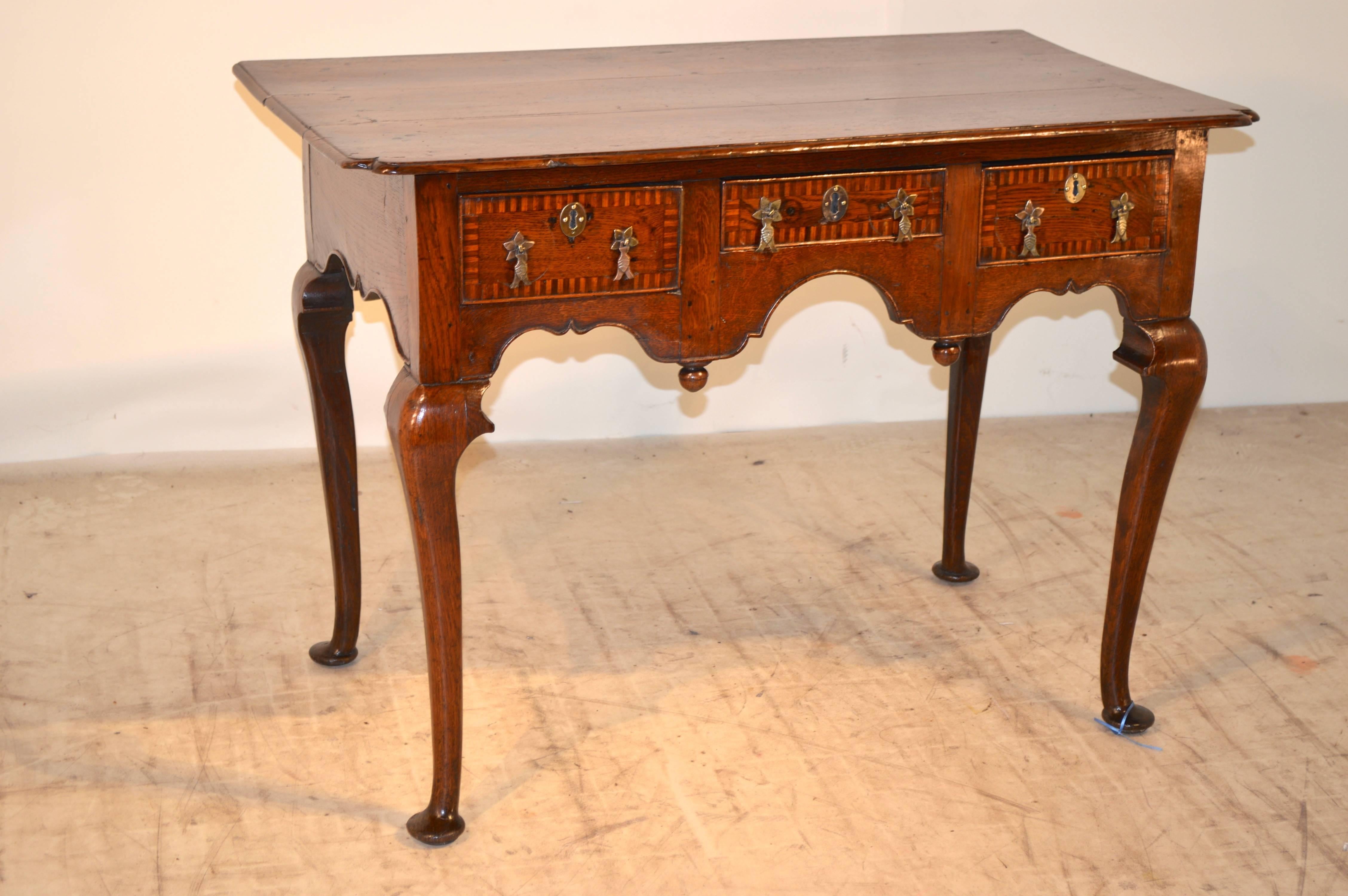 Early 18th century English lowboy from the Georgian period. The top is made up of three boards which have bevelled edges and scalloped front corners. The scalloped apron contains three drawers, which have beading and inlaid borders, and is decorated