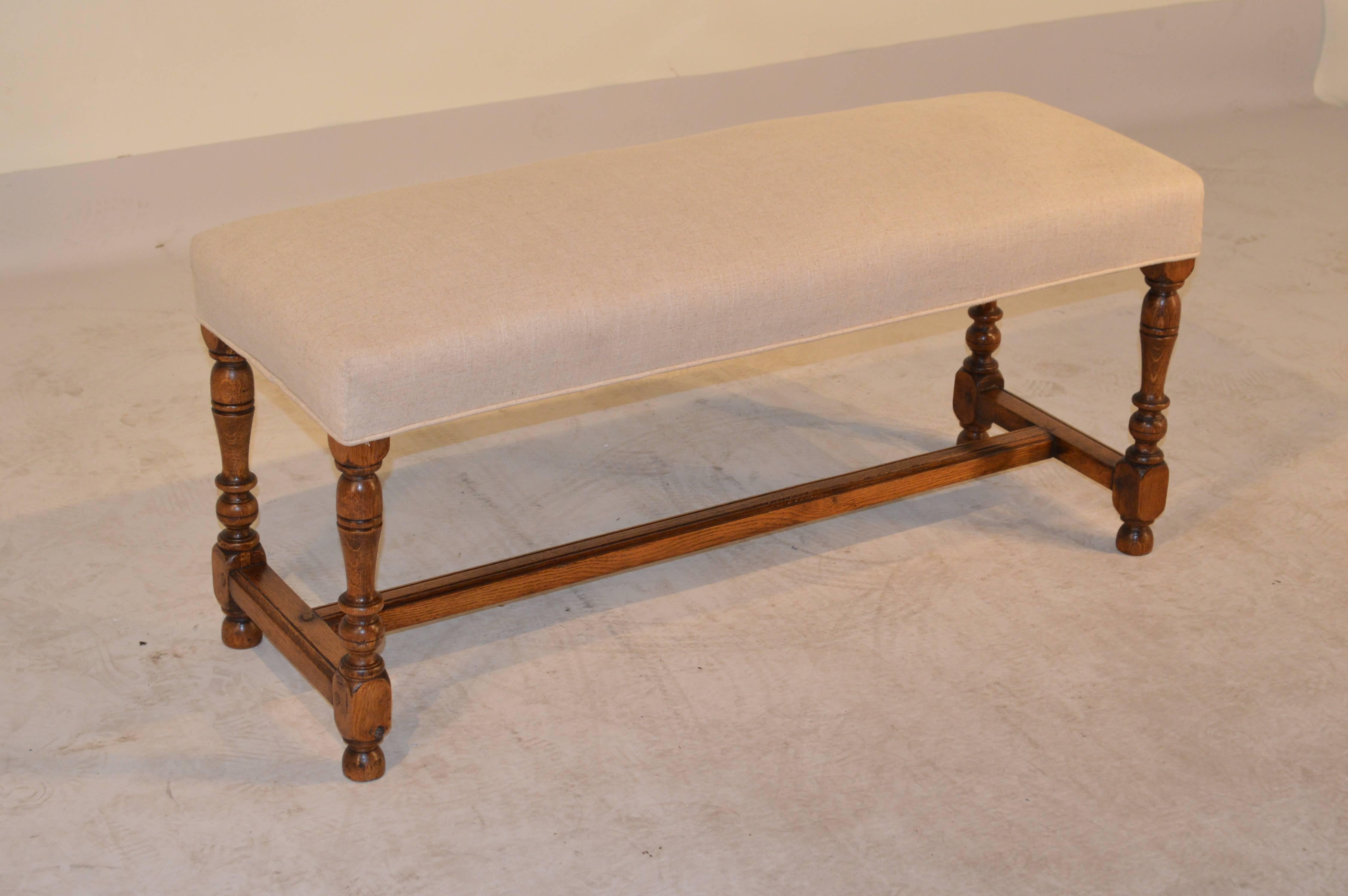 19th century English oak bench with hand-turned legs, joined by simple stretchers and cross stretcher, and raised on turned feet. The seat has been newly upholstered in linen and finished with single welt decoration.