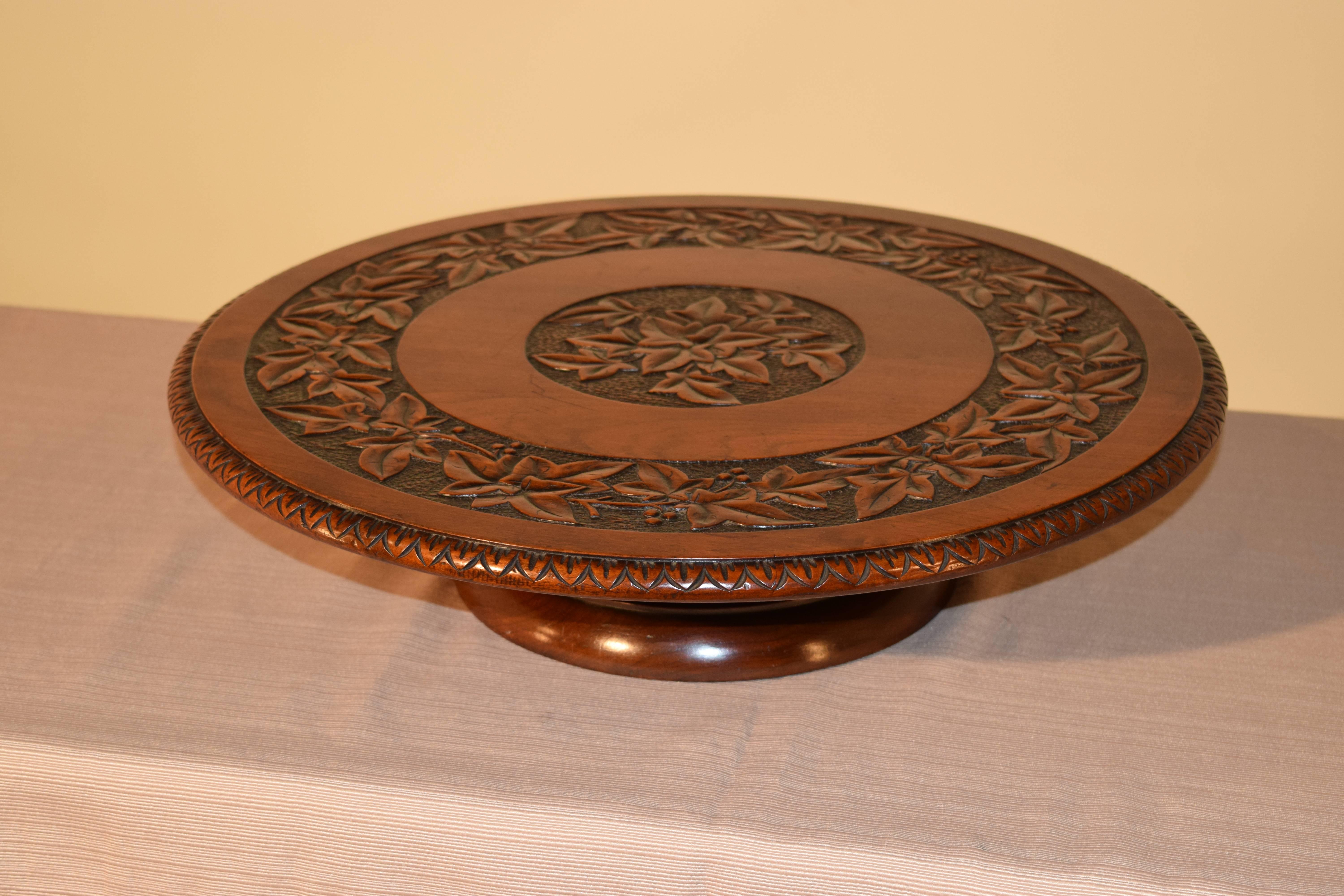 19th Century lazy Susan made from Mahogany. The top is carved with a central medallion and a band around the edge depicting leaves. The edge of the top is beveled and carved decorated as well. It is supported on a hand turned base.