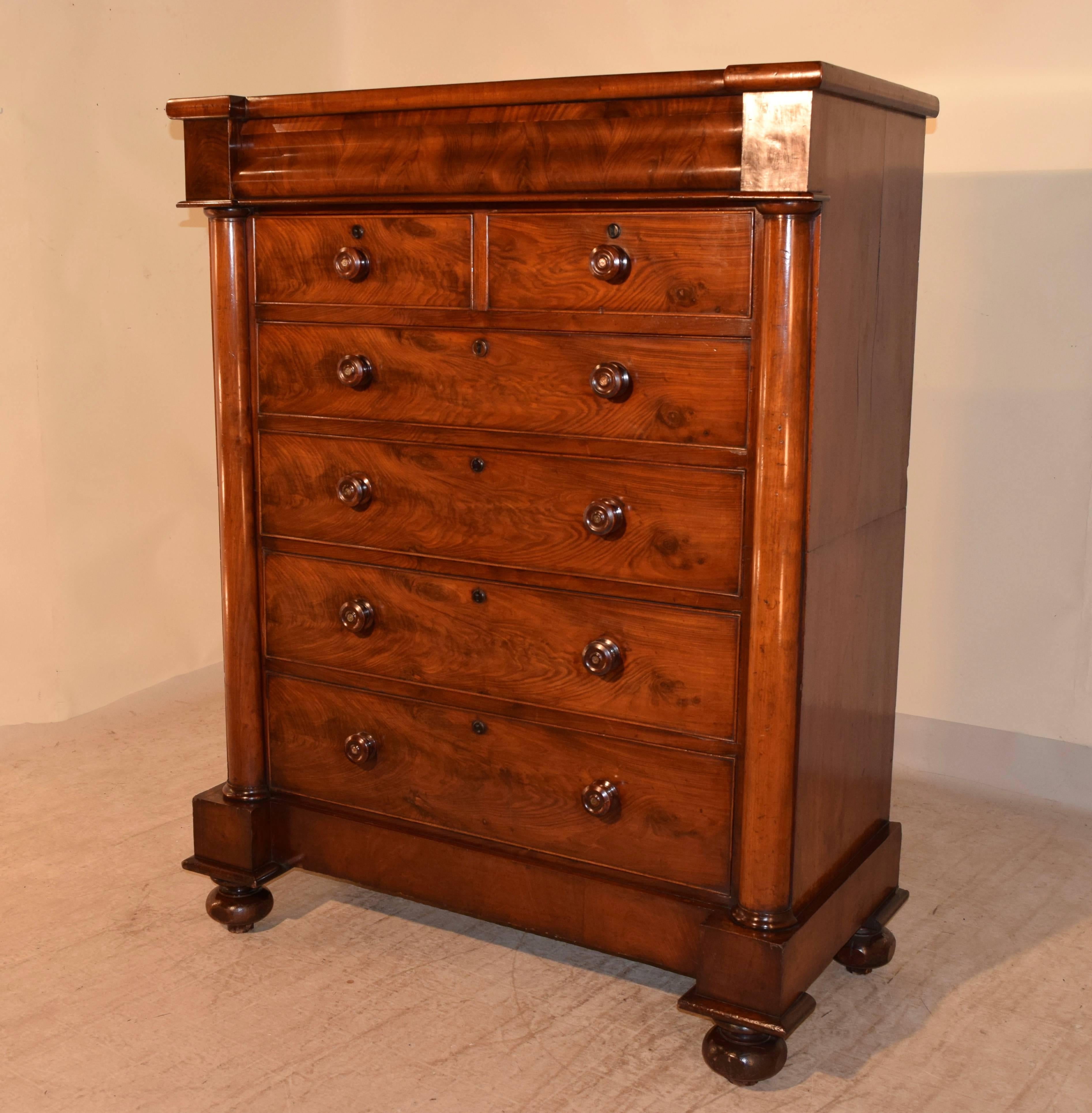 19th century large chest of drawers made from mahogany. The top is shaped and has a hidden drawer. The top molding pulls out and reveals a concealed drawer. It has two drawers over four drawers, flanked by half round columns with turned caps on the