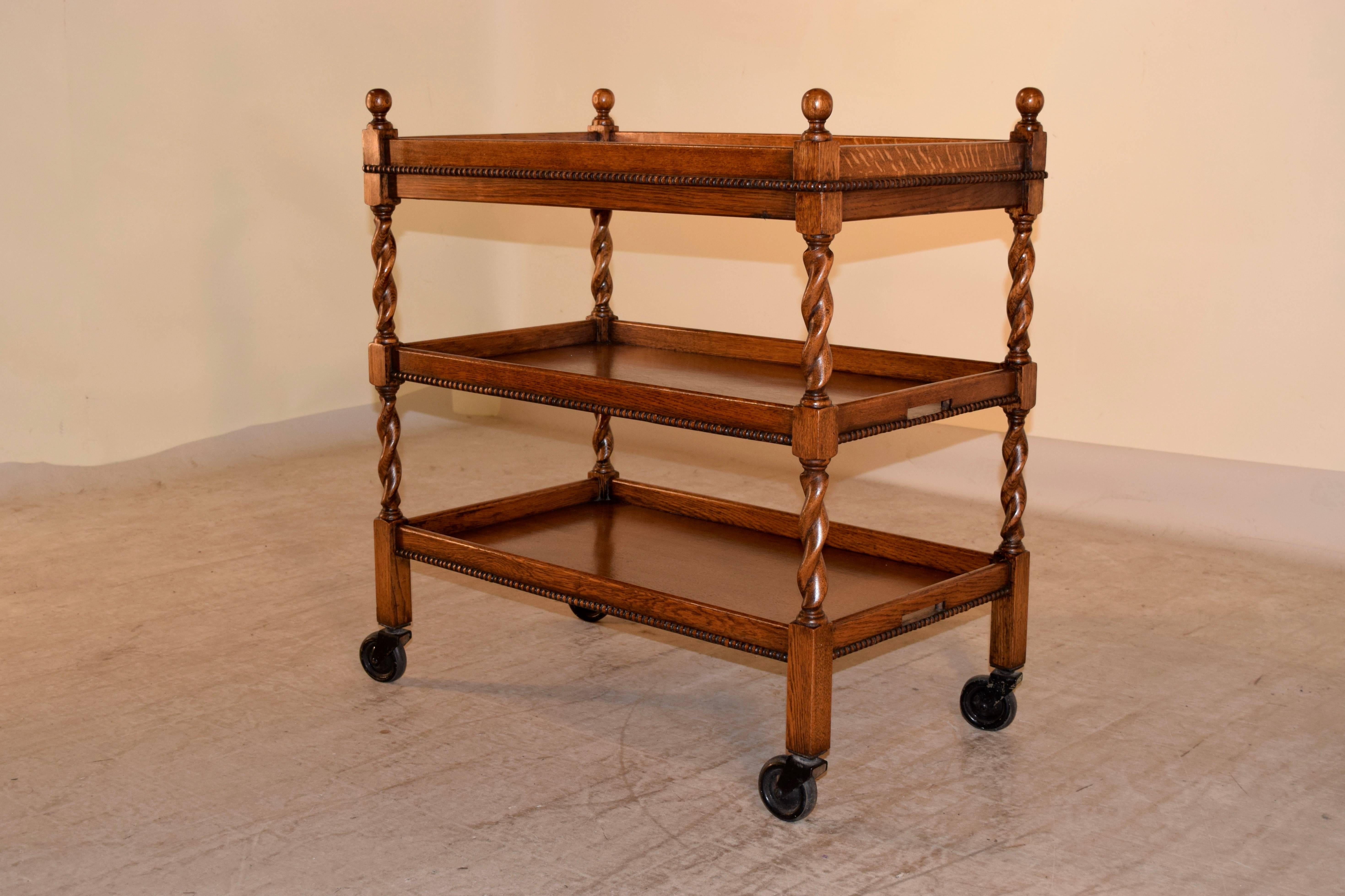 English oak drinks cart, circa 1900. The top is decorated with finials, following down to three shelves, all with galleries around the edges and beading. They are joined by hand turned legs and are supported upon original casters.