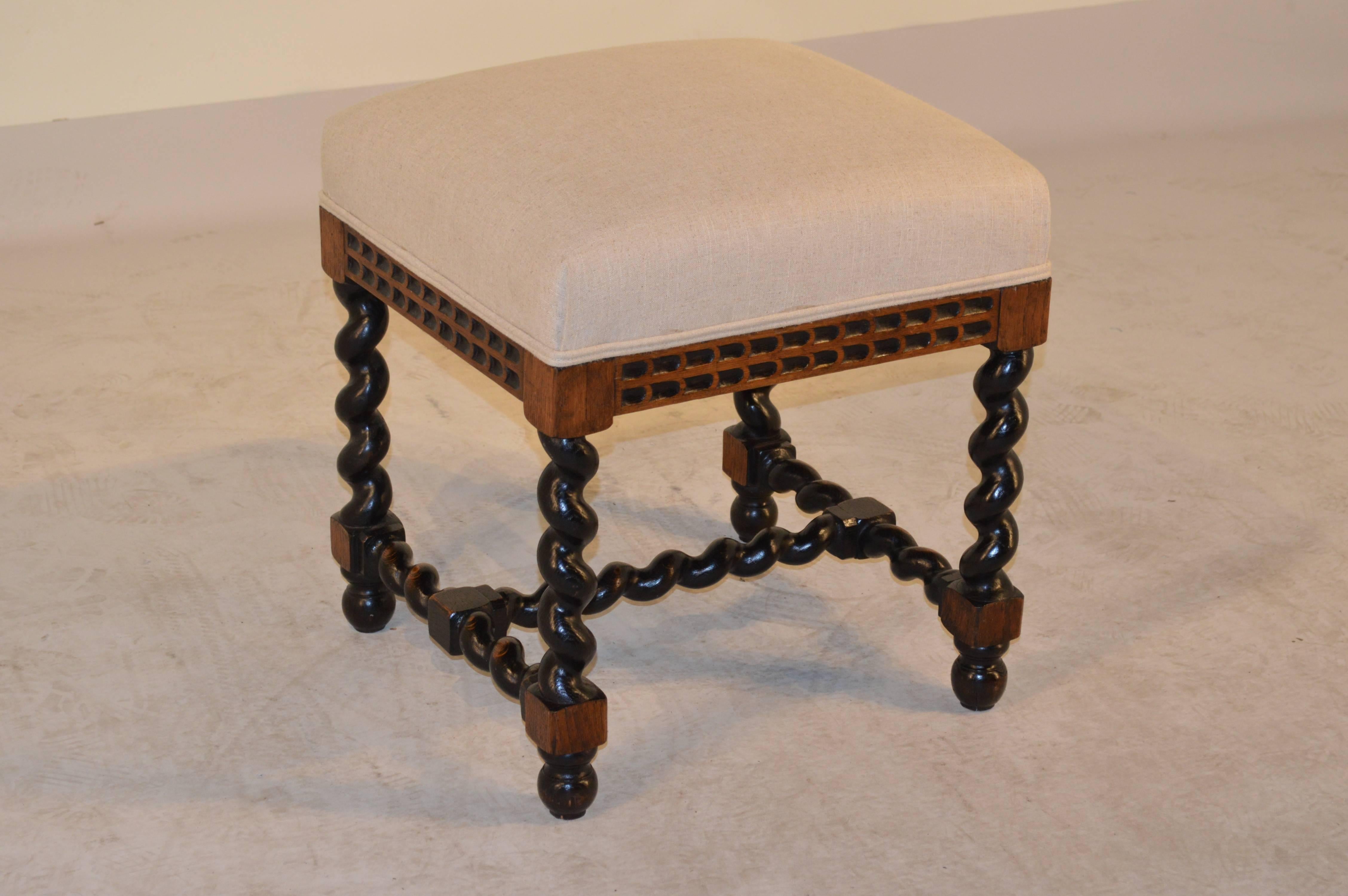 19th century English oak stool with a hand-carved decorated apron and supported on hand-turned barley twist legs, joined by stretchers and a cross stretcher. Raised on turned feet. The seat has been newly upholstered in linen and finished with a