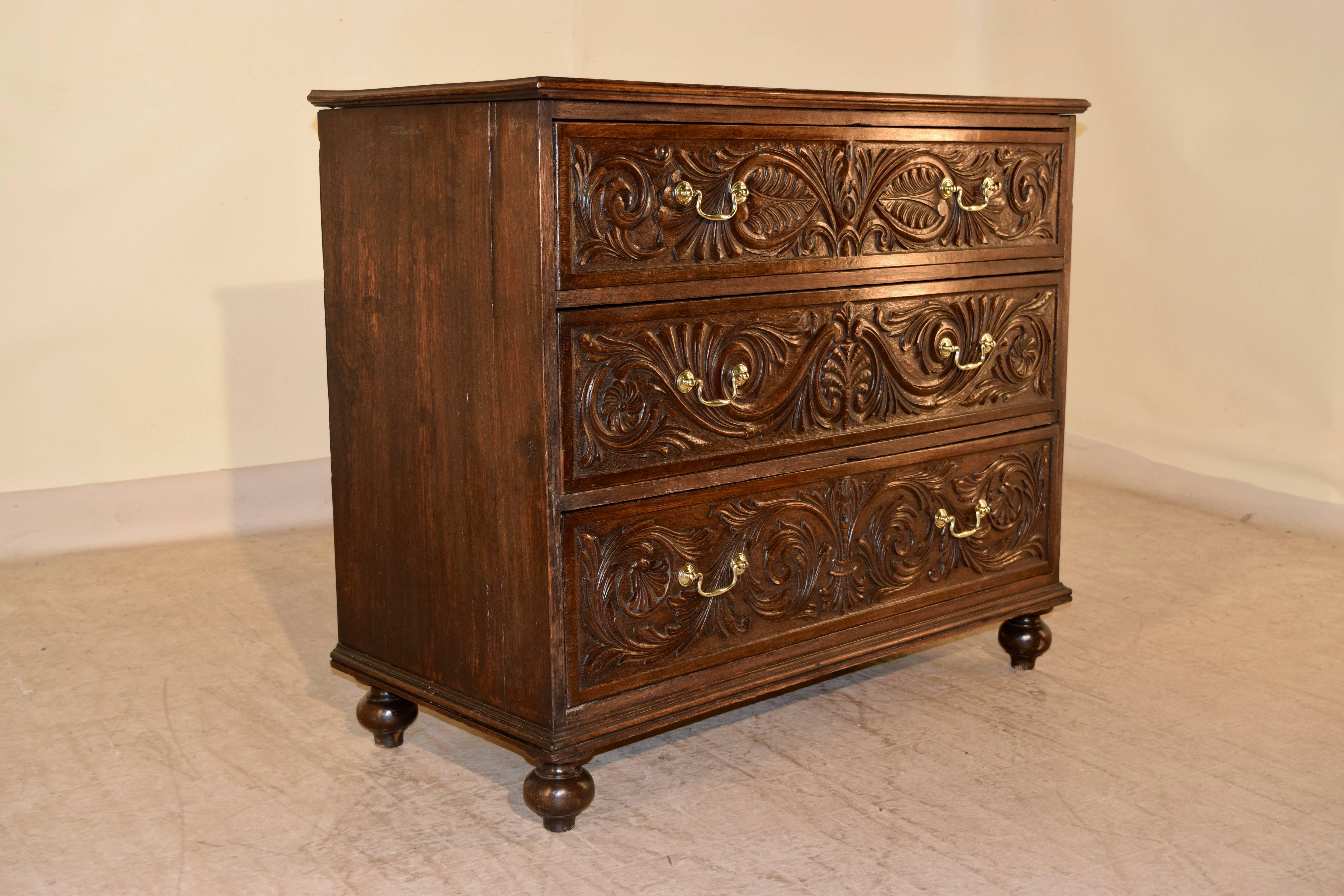 Early 19th century English oak chest of drawers with a beveled edge around the top, following down to three drawers with hand- carved decorated drawer fronts. The sides are simple and have age shrinkage. The case is raised on turned feet.