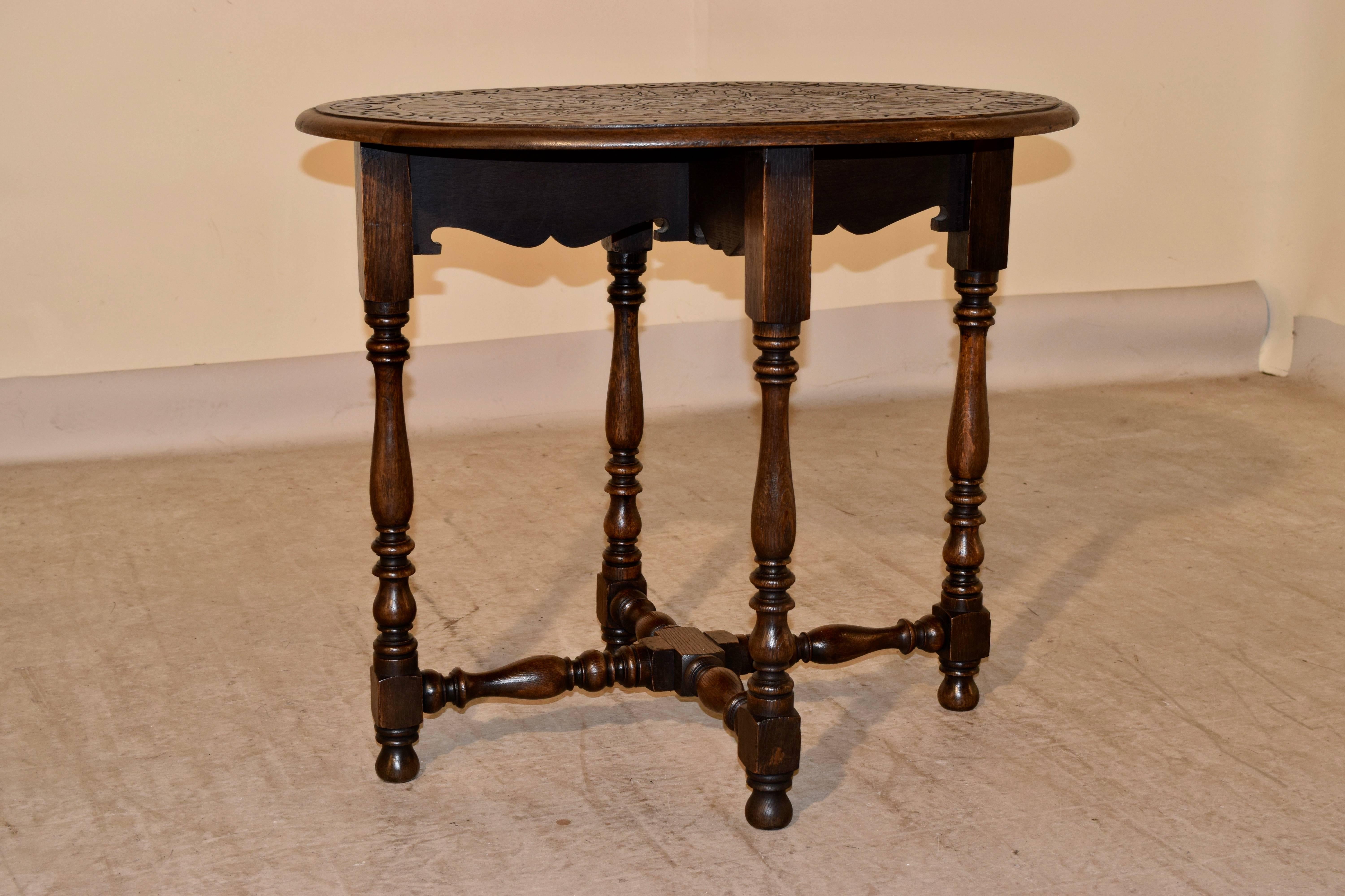 19th century oval oak side table from England. The top is carved in a leaf pattern on the top and has a carved decorated banded edge which is also beveled. The apron is scalloped, and has hand-turned legs joined by hand-turned cross stretchers.
