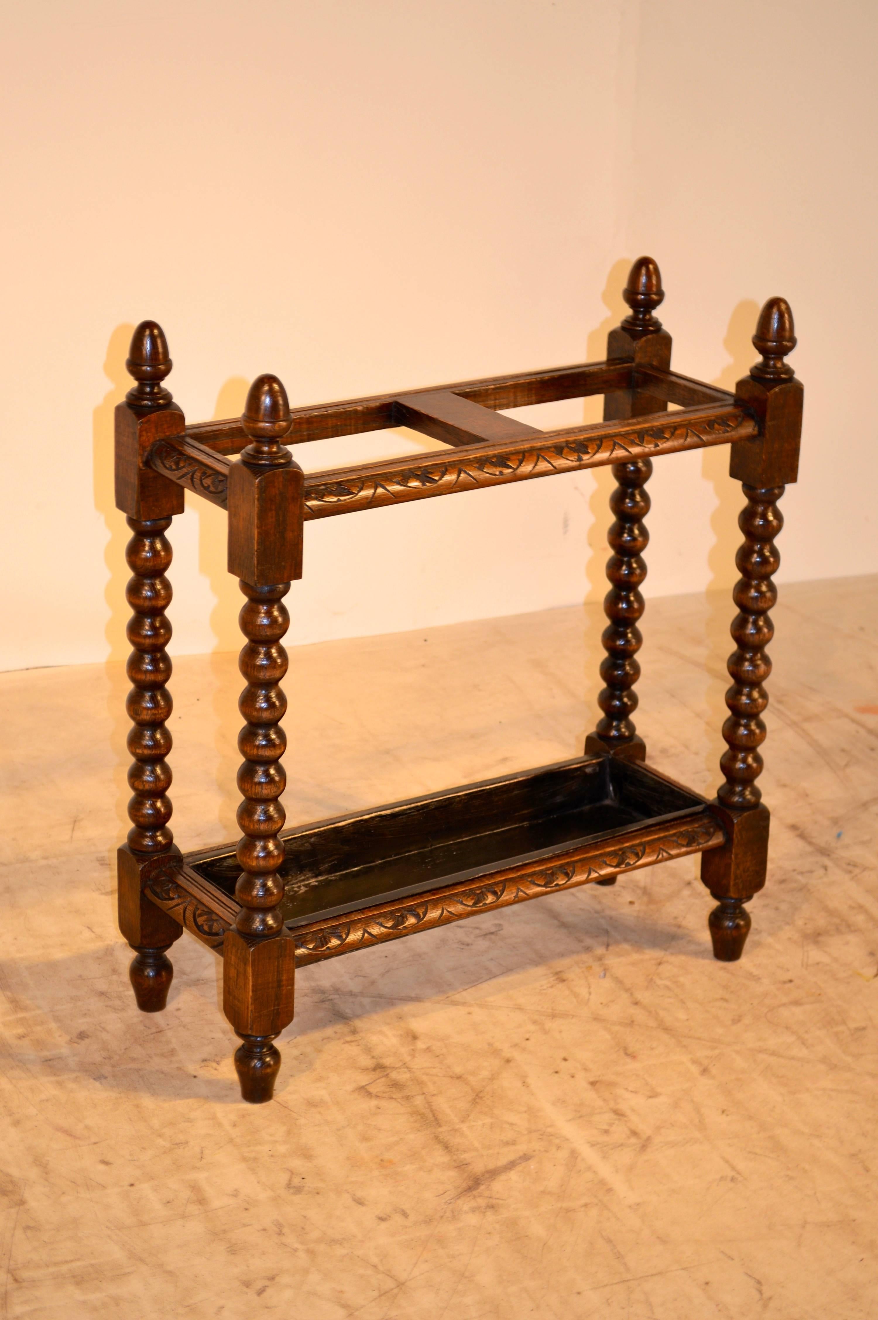 English oak umbrella stand with four acorn turned finials, carved decoration throughout, and hand-turned spool legs; circa 1880. Raised on turned feet.