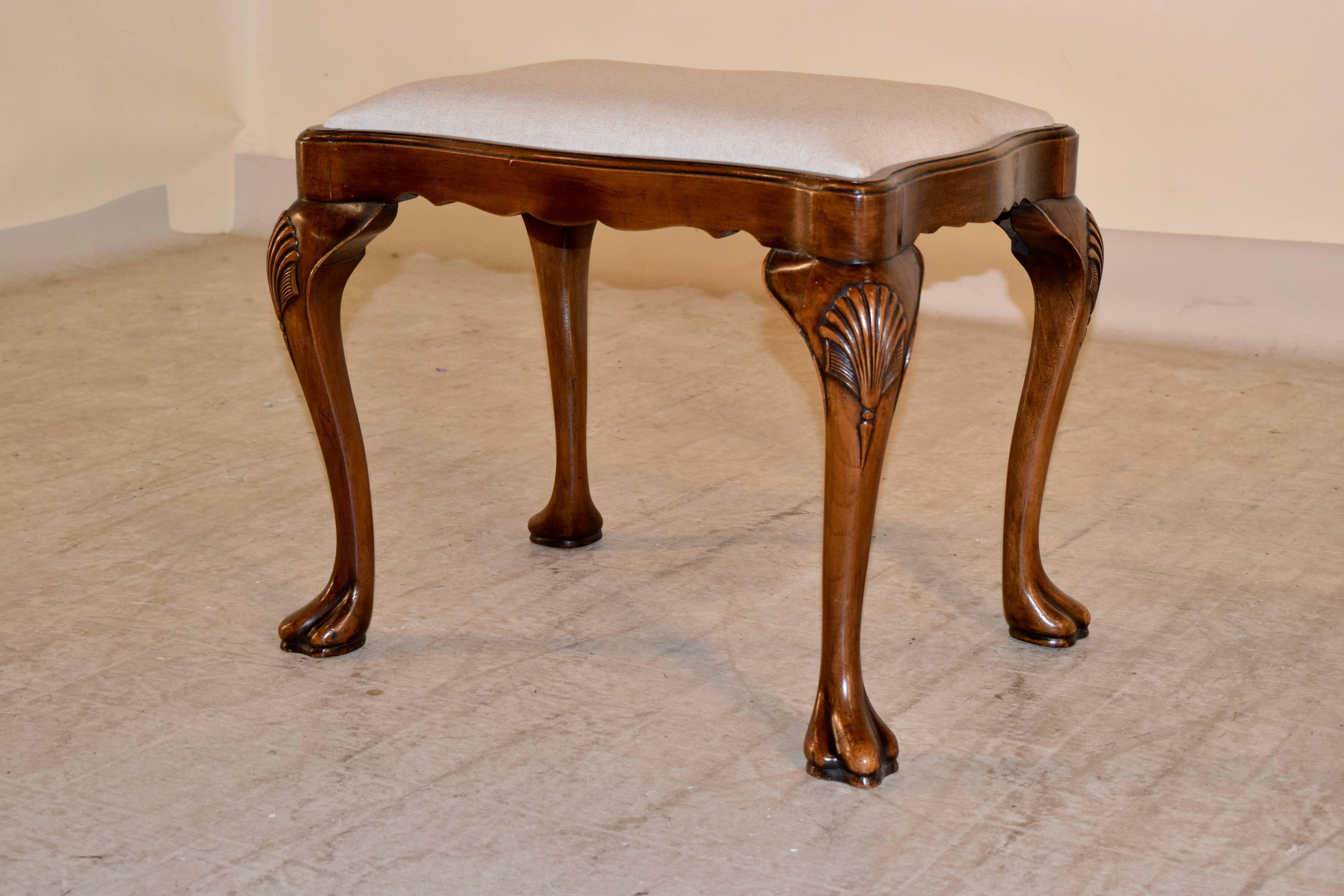 19th century English stool made from walnut. The seat has been newly upholstered in linen and is serpentine in shape, following down to a wonderfully hand scalloped apron and graceful cabriole shaped legs with carved shells on the knees and ending