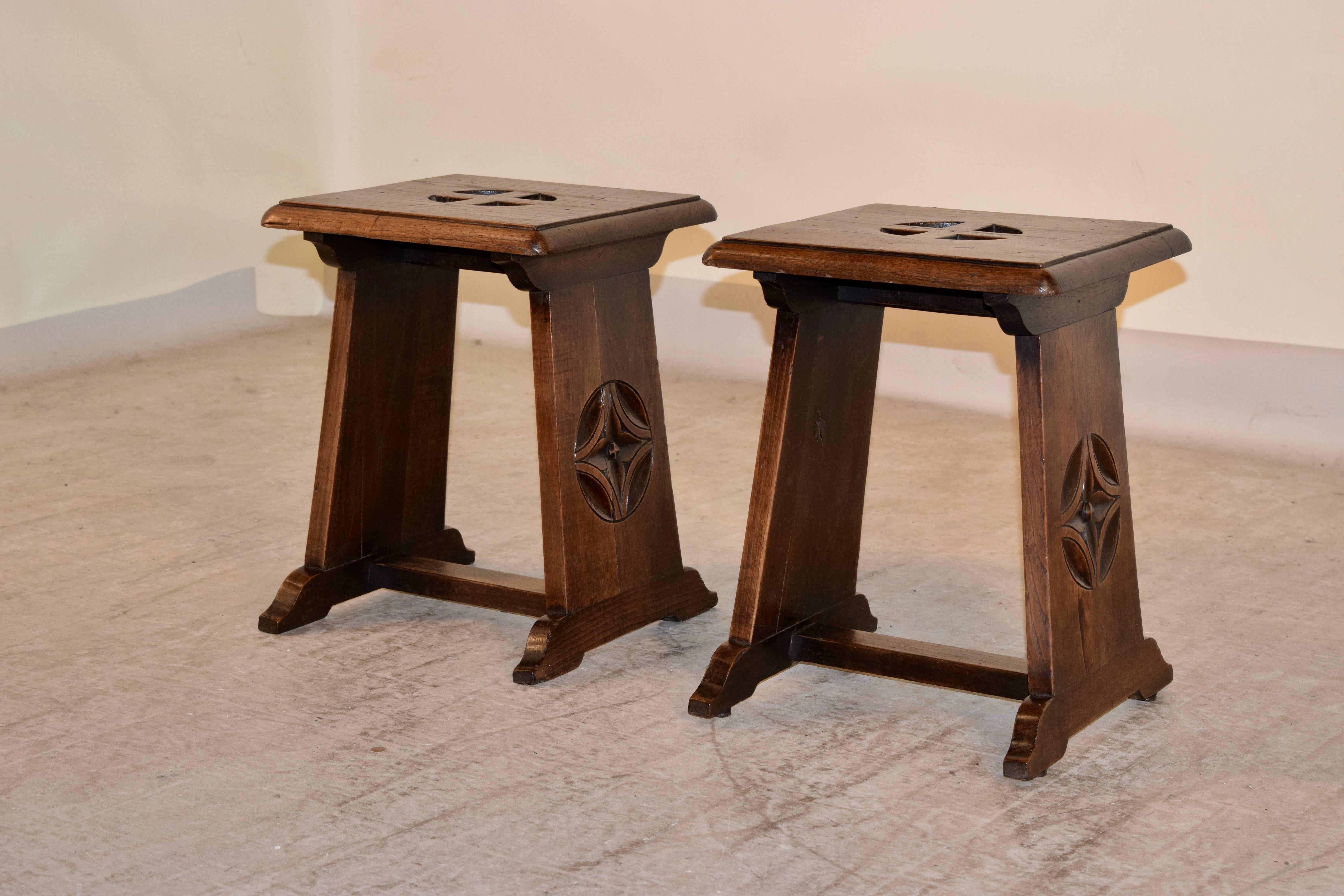 19th century, pair of English oak stools in the Gothic Revival style. The tops have pierced decorations and beveled edges and are supported on trestle legs with carved decorations and joined by cross stretchers.