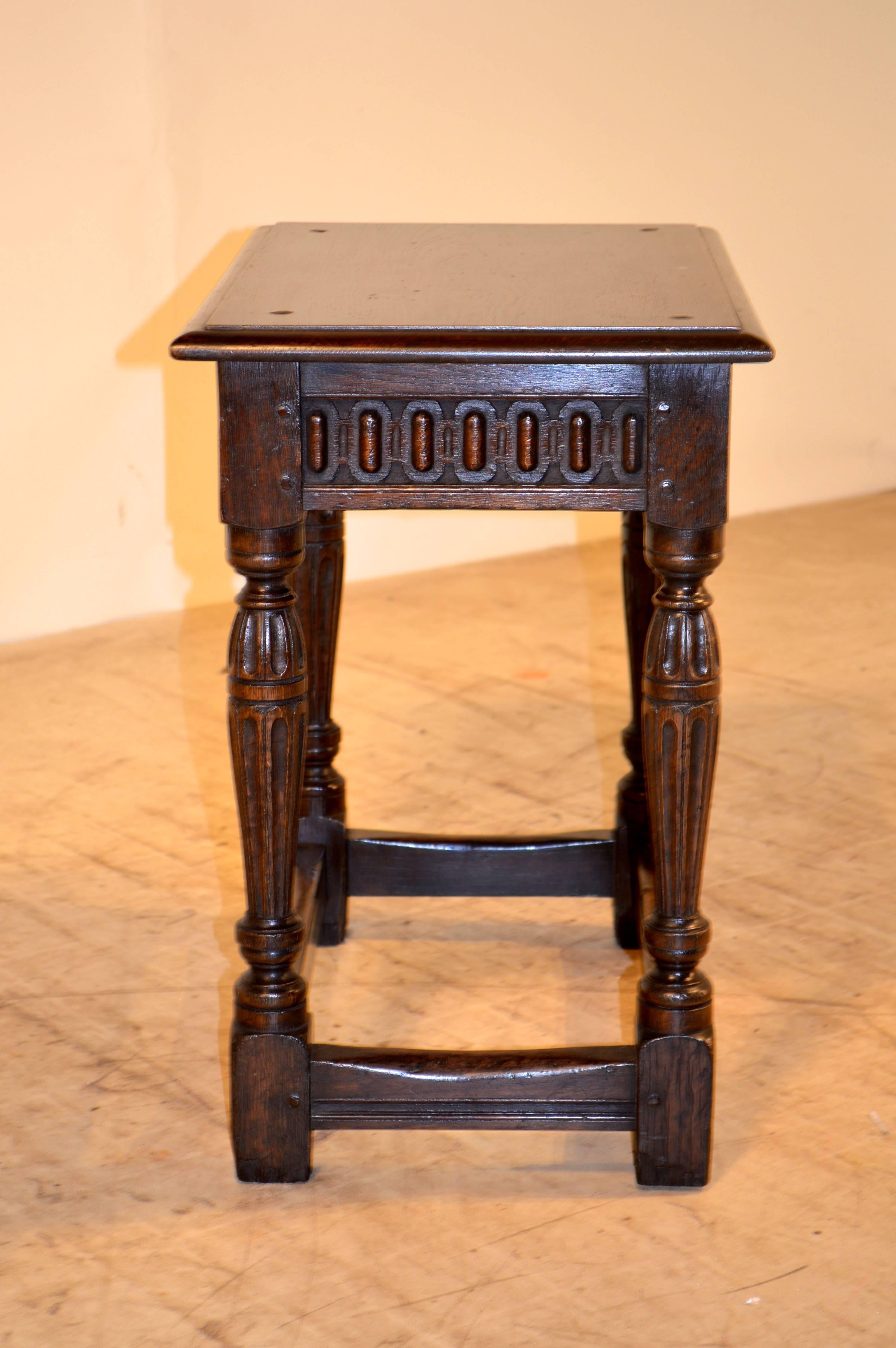 Large 19th century English oak joint stool with pegged construction and a beveled edge around the top. The apron has carved decoration and follows down to fluted carved legs joined by stretchers.