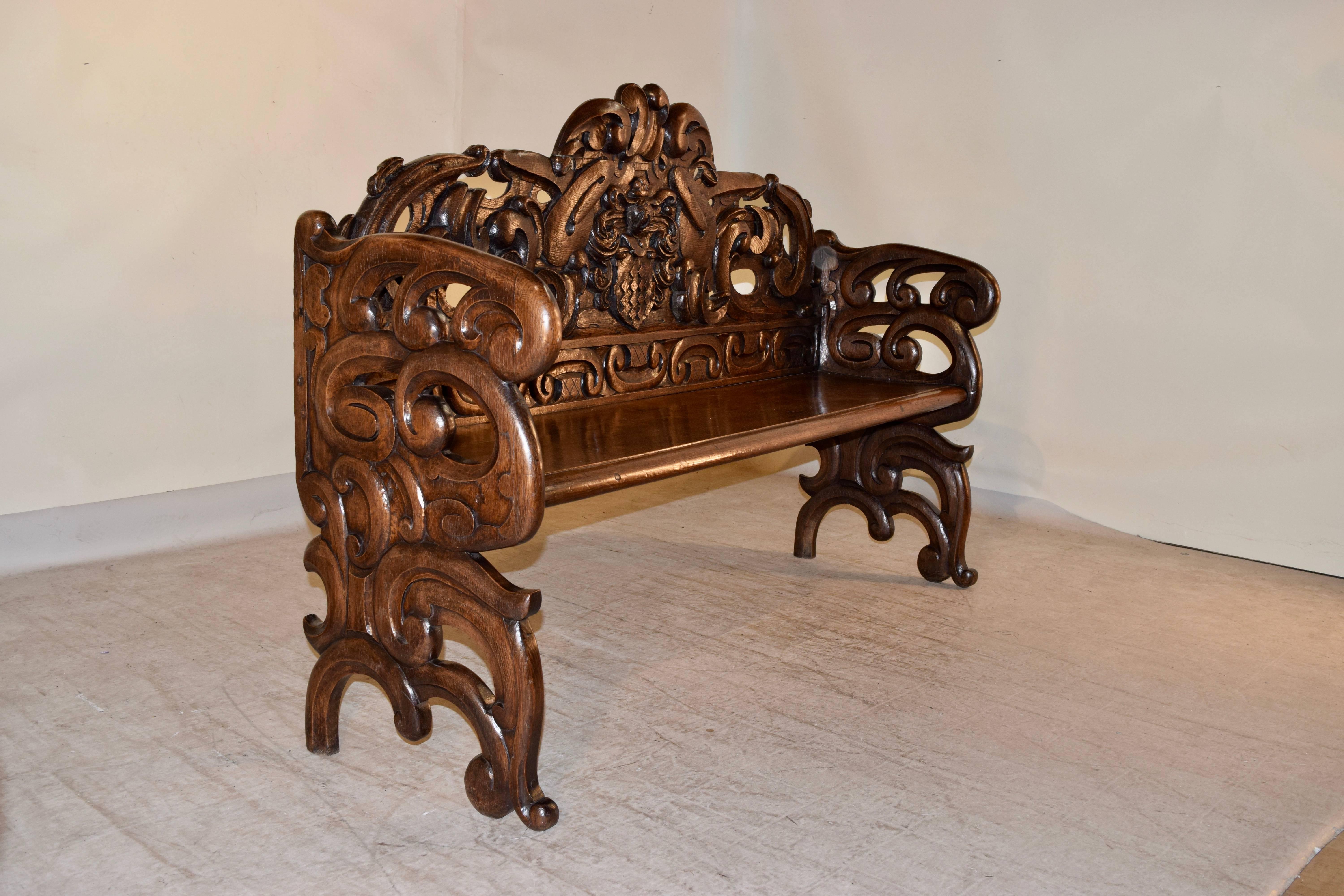 19th century French bench made from oak. The back is exquisitely hand-carved with a central coat of arms, surrounded by decorative carvings. The sides are made up of matching decorative pierced carvings. The seat has a beveled front edge, and the