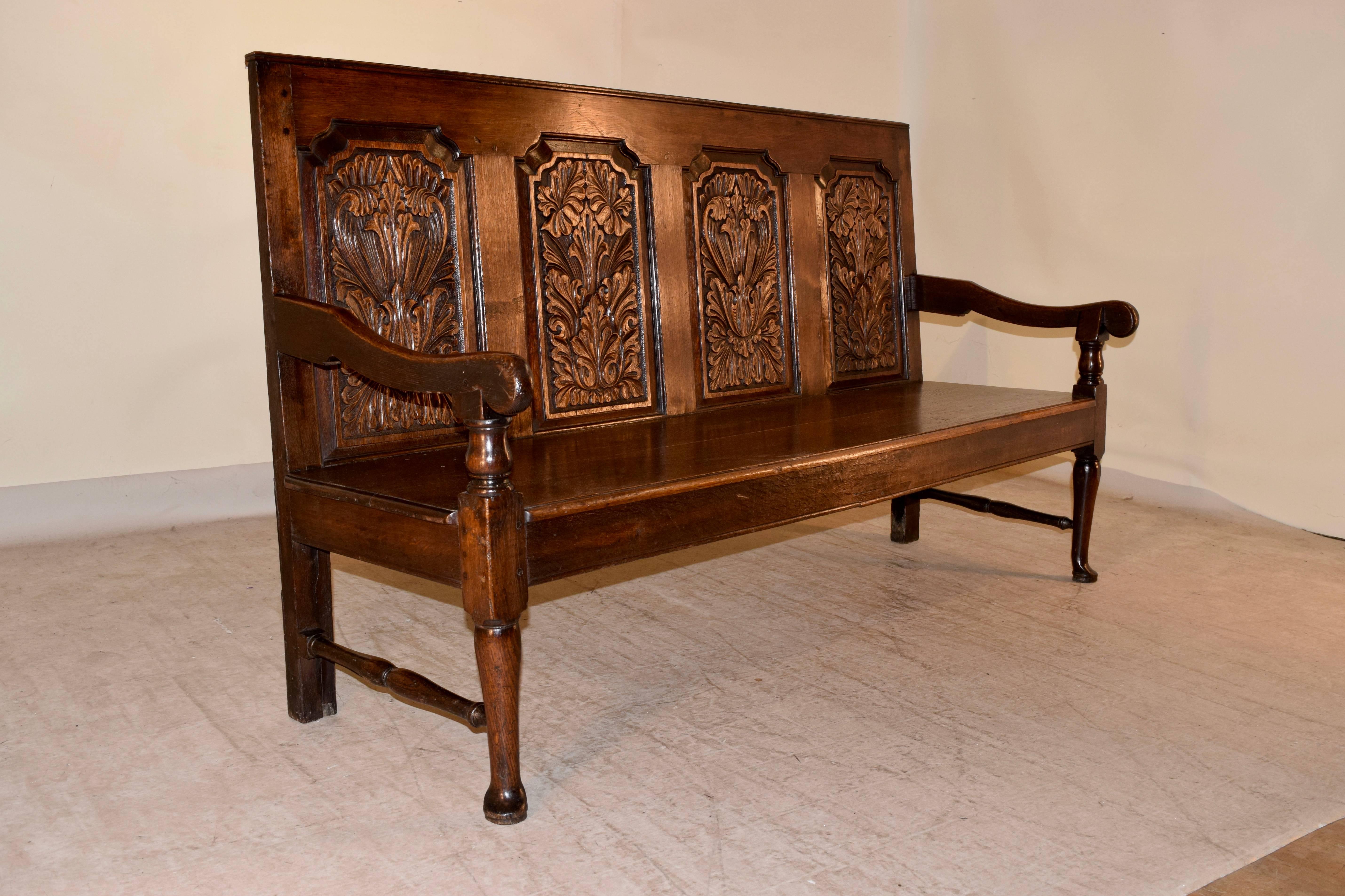 18th century English oak bench with a paneled back, which has four hand-carved shaped molded raised panels with acanthus leaf decoration. The seat is made up of two planks, and is beveled along the front edge. The arms are also shaped and the piece