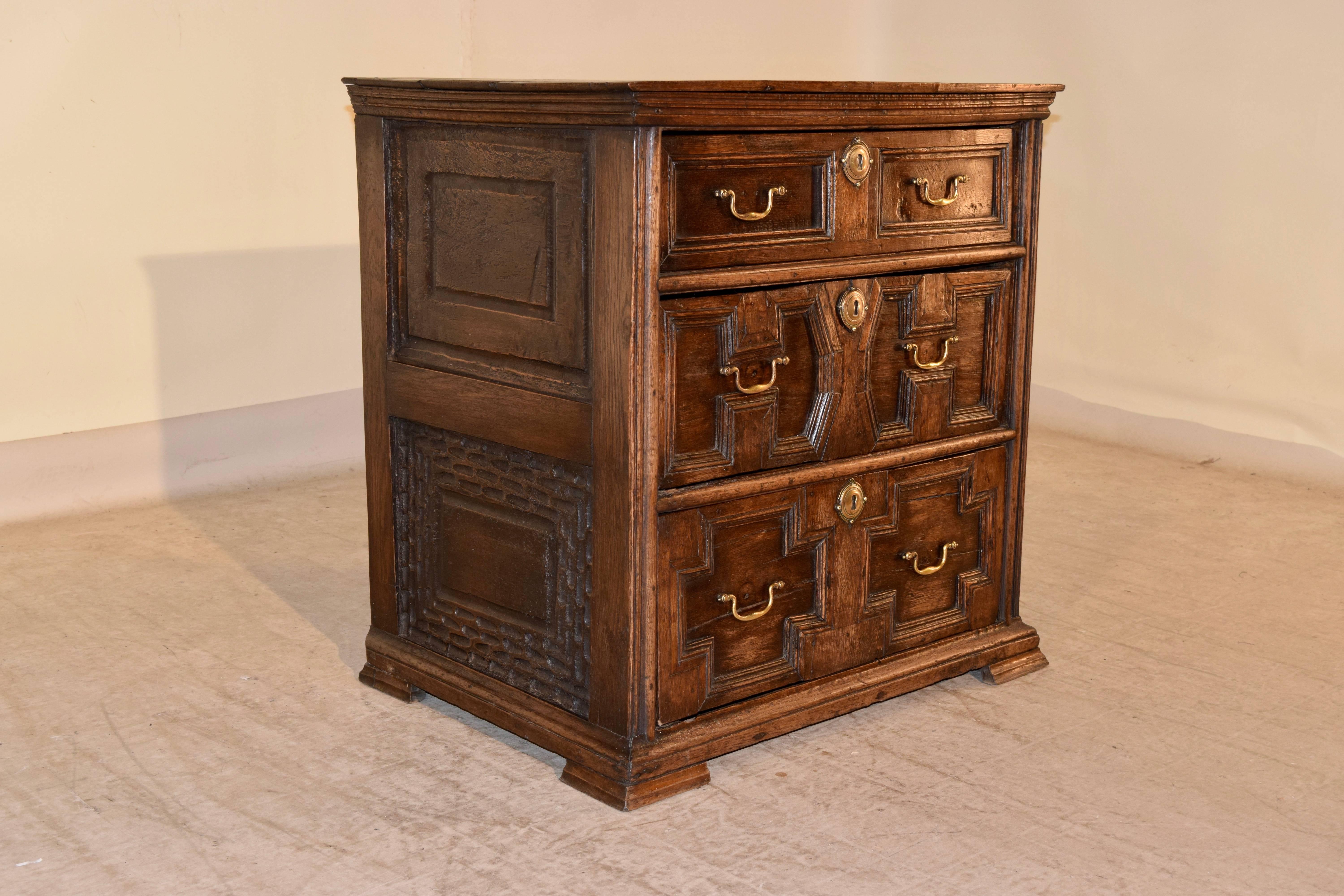 English oak chest of drawers with a plank top, following down to raised paneled sides, the lower panel is wonderfully hand carved as well, circa 1720. The case has three drawers, which are also raised paneled with geometric panels. The piece is