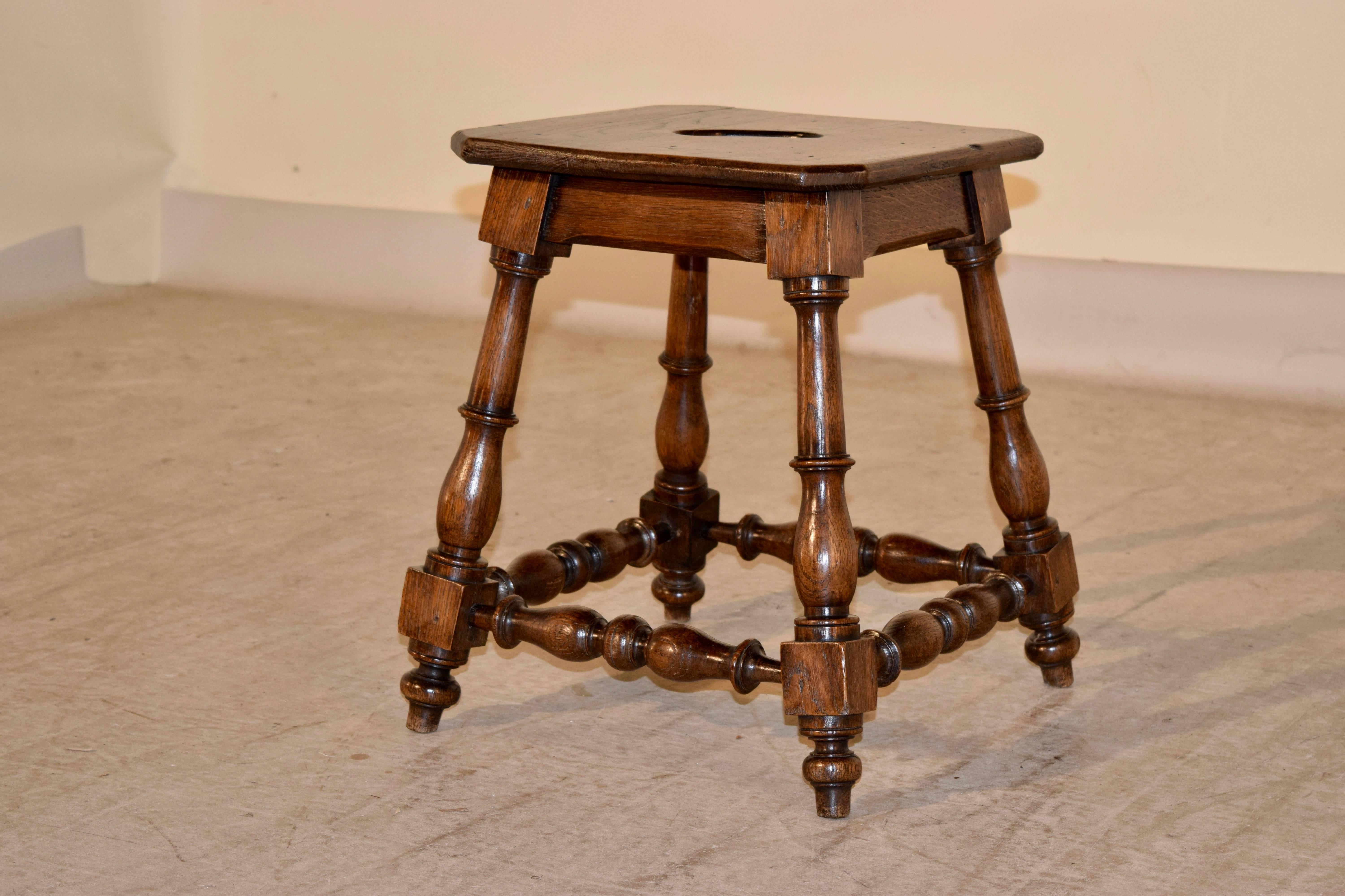 19th century oak stool from France with a two plank top, which has a handle cut-out. It has a simple apron and is supported on splayed turned legs, joined with turned stretchers.