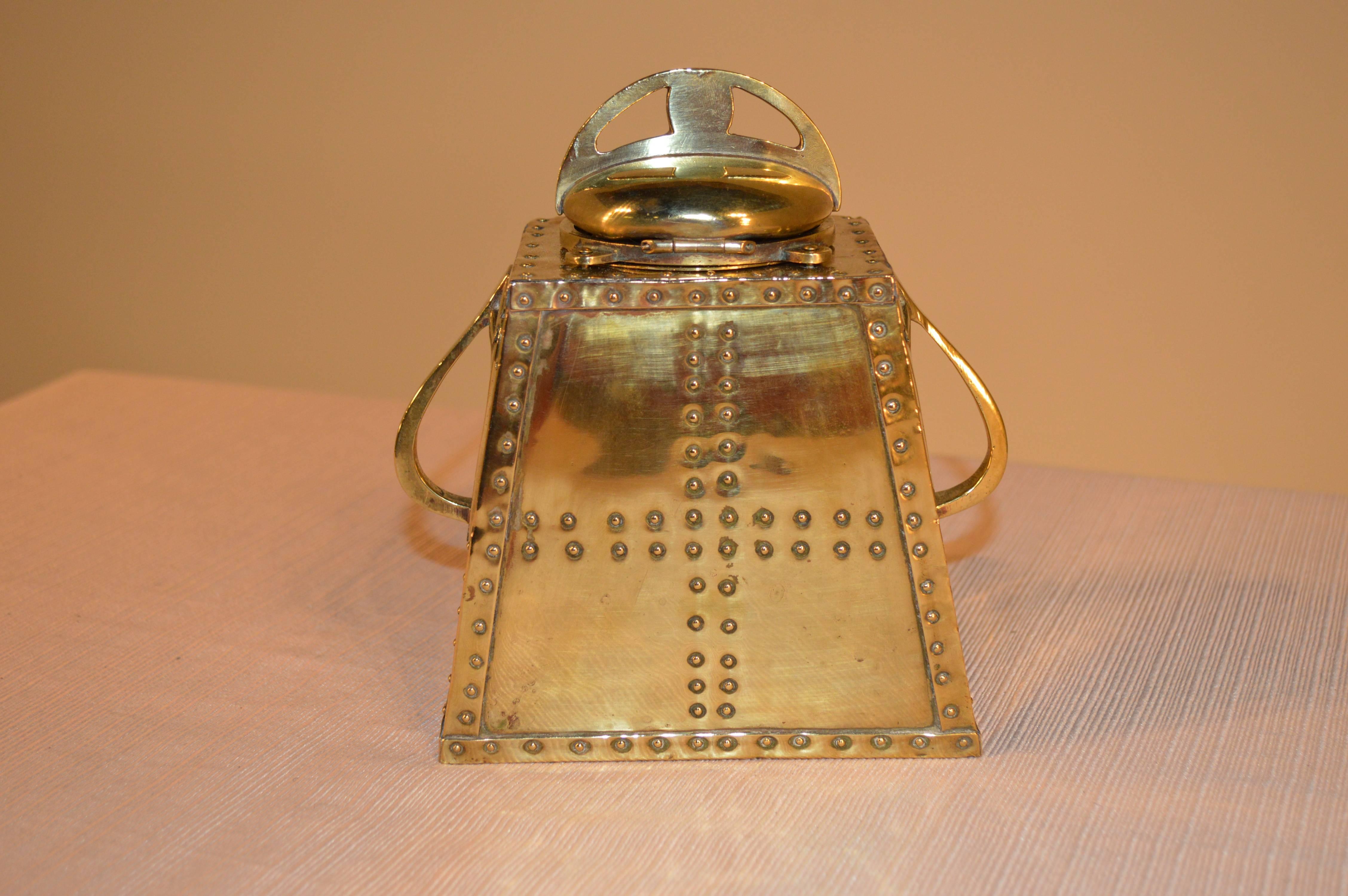 Late 19th century brass inkwell. The top lifts to reveal a porcelain inkwell. The base is detailed with rivets and on the front has a horses profile surrounded by a horseshoe, with a pen rest below.