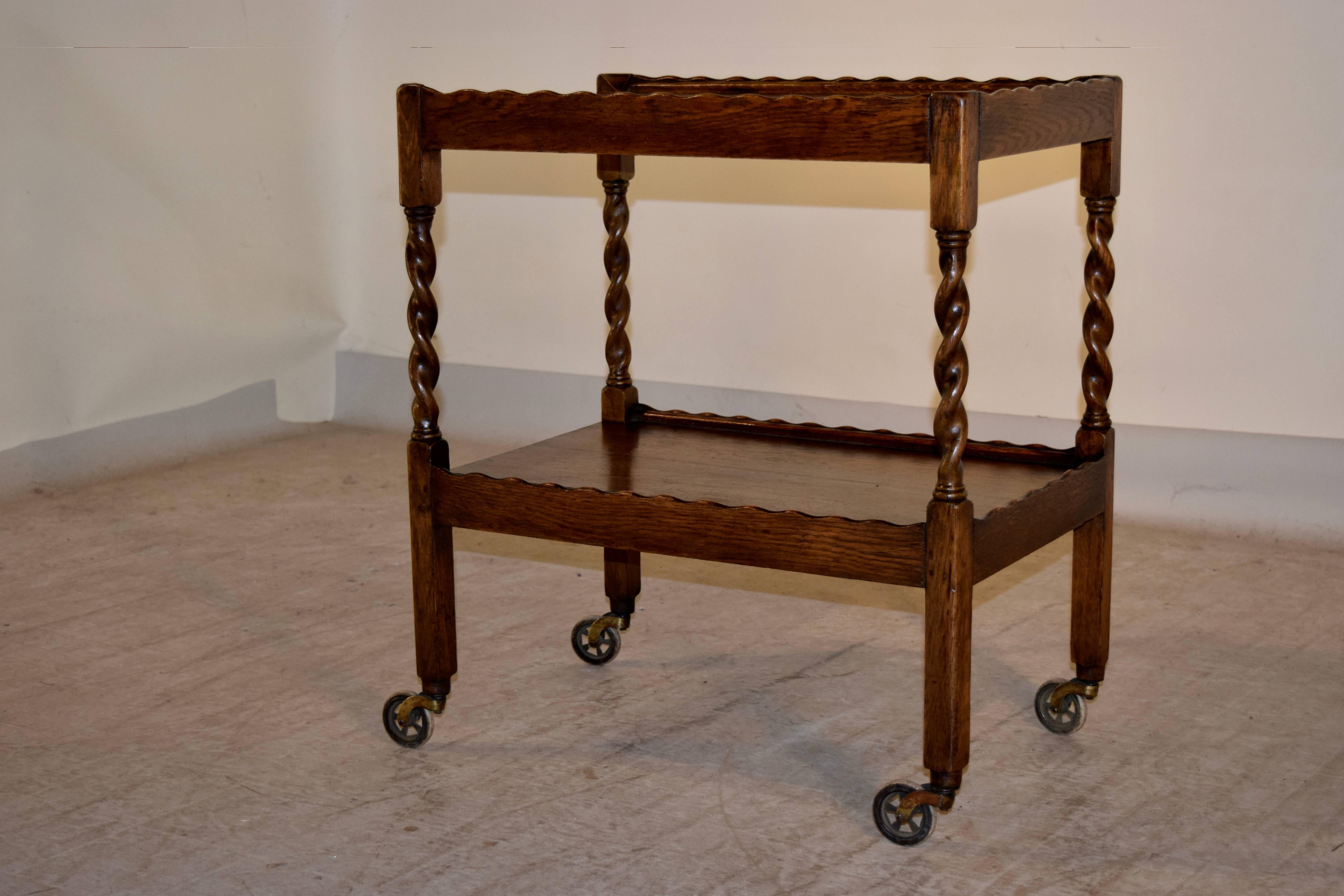 English oak drinks cart with scalloped galleries around the top and lower shelves, which are connected by barley twist legs, circa 1900. Supported on casters.