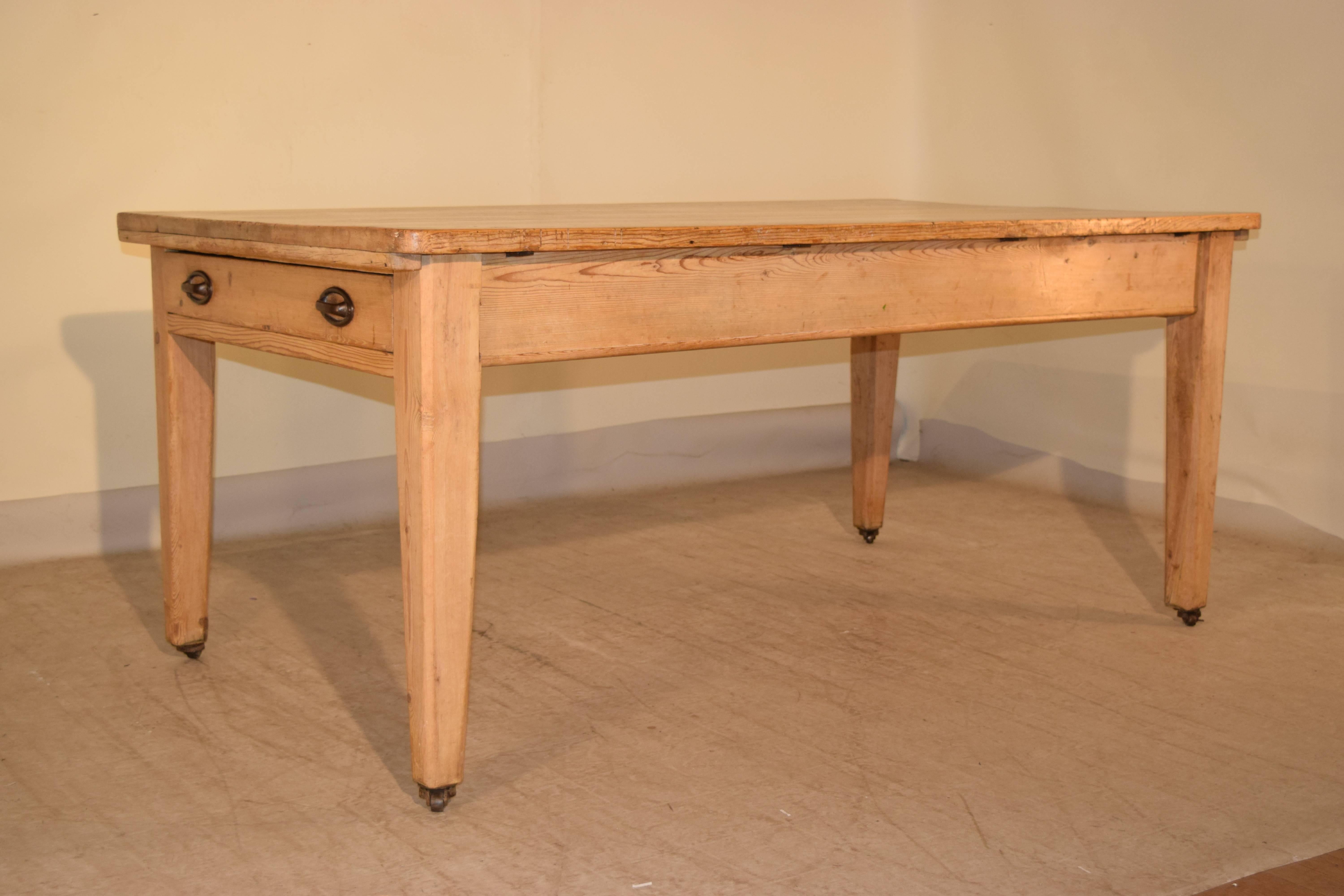 19th century English work table made of pine. The top is made up of scrubbed planks and follows down to a simple apron, which has two drawers, one on each end. It is supported on slightly tapered legs, ending in casters. The top is 1