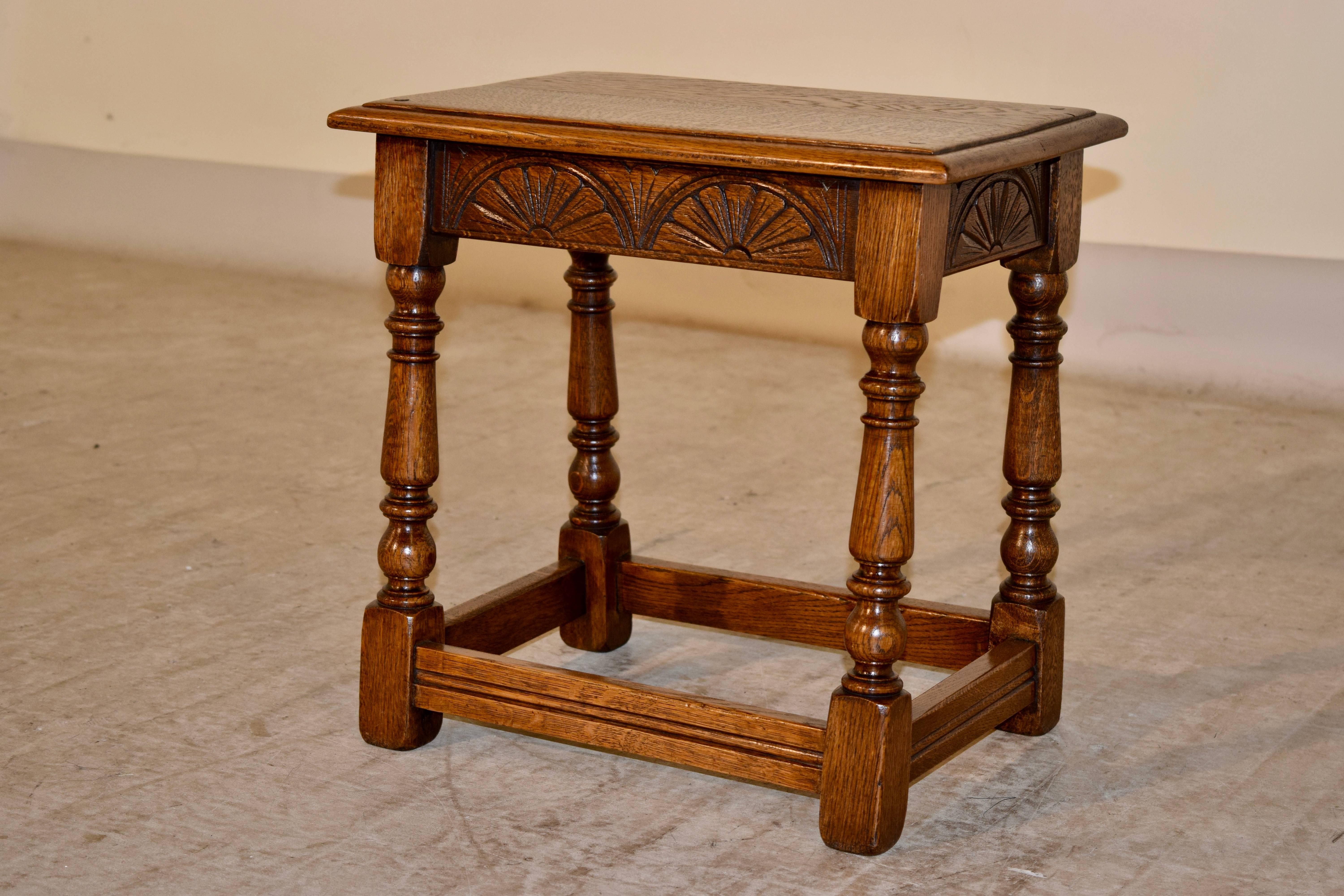 English oak joint stool, circa 1900, with a beveled edge around the top and pegged construction. It has a carved apron on all four sides, and is supported on turned legs, joined by simple stretchers.