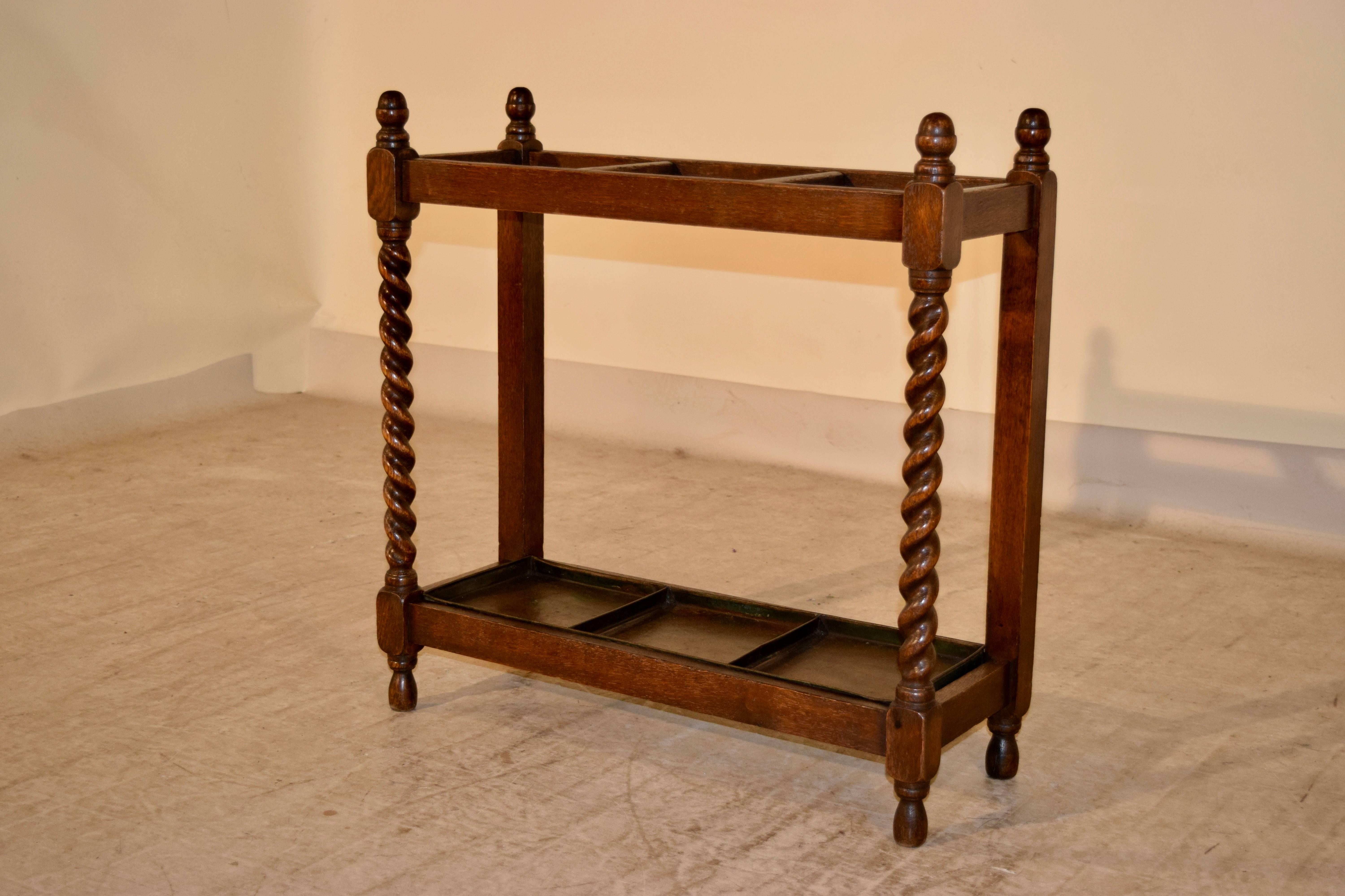 Late 19th century English oak umbrella stand with finials on the top, following down to hand-turned barley twist legs in the front and simple legs in the back for easy placement against a wall. It retains what appears to be the original tray and is