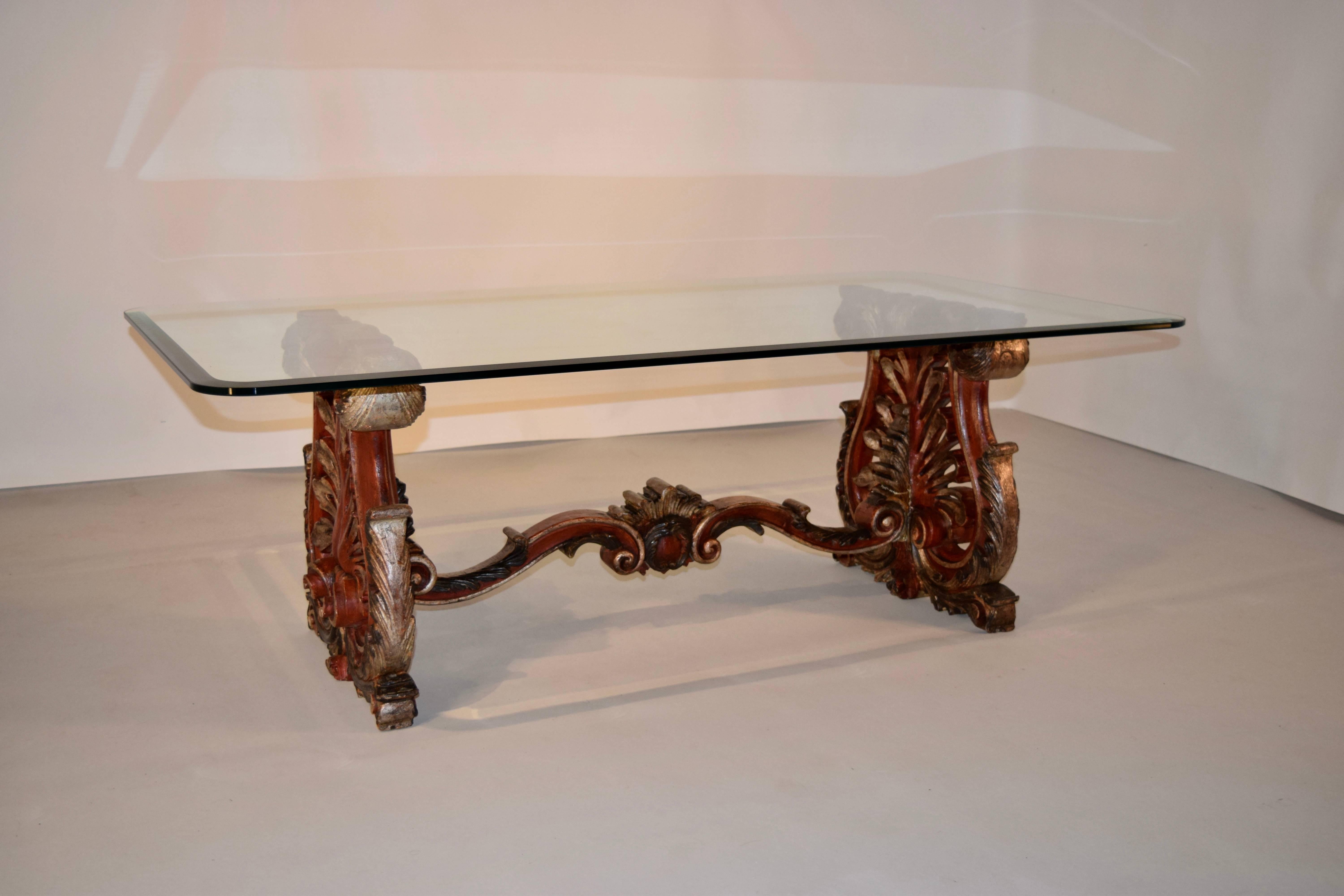 19th century hand-carved and painted wooden coffee table from Italy. The end supports are trestle shaped and are finely carved with acanthus leaves and pierced decoration over a carved scroll foot. The top is glass, and has a beveled edge and