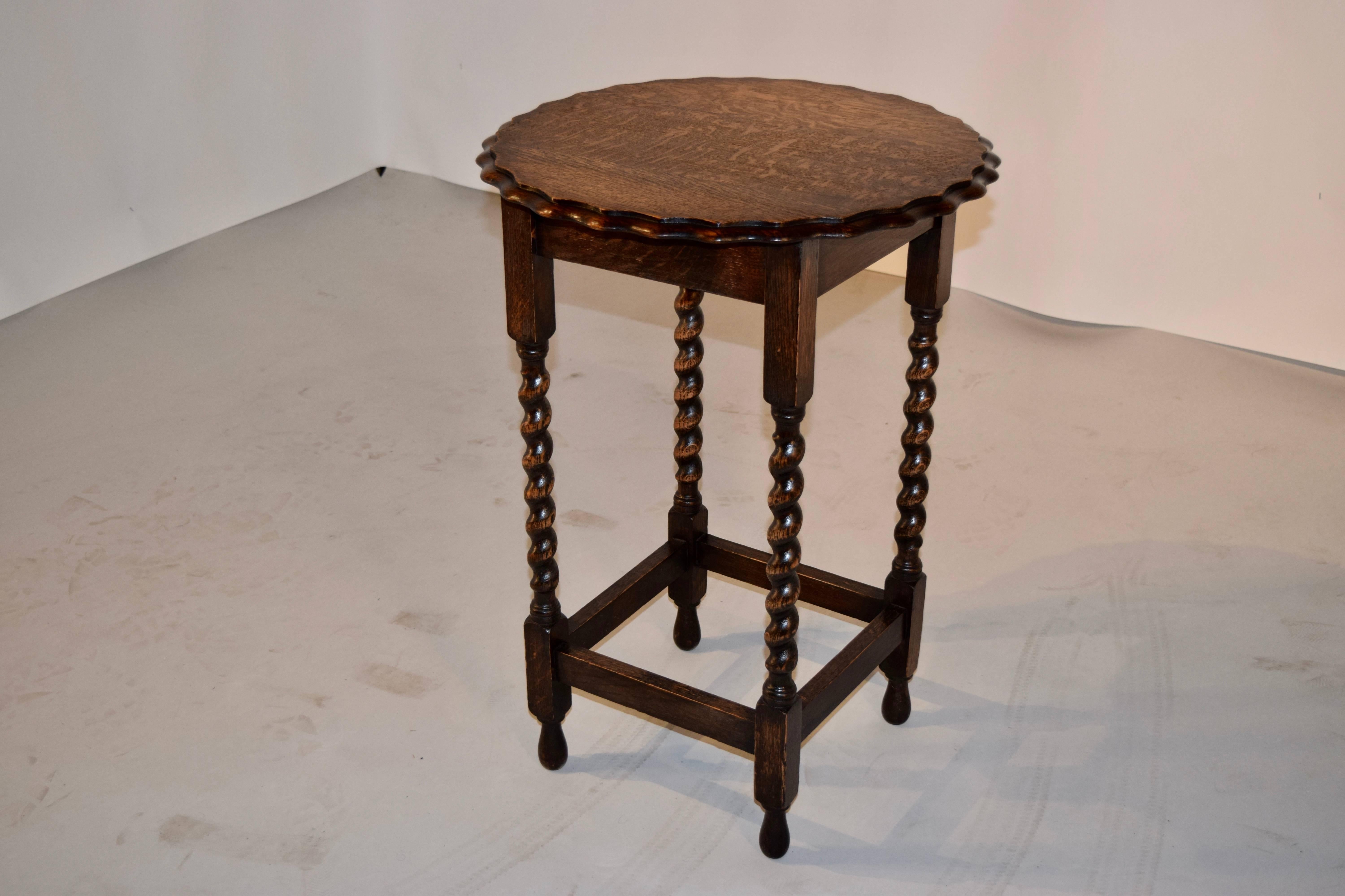 English oak side table with a round top which has a scalloped and beveled edge around the top, following down to a simple apron and hand-turned barley twist legs, joined by simple stretchers. Raised on hand-turned feet.