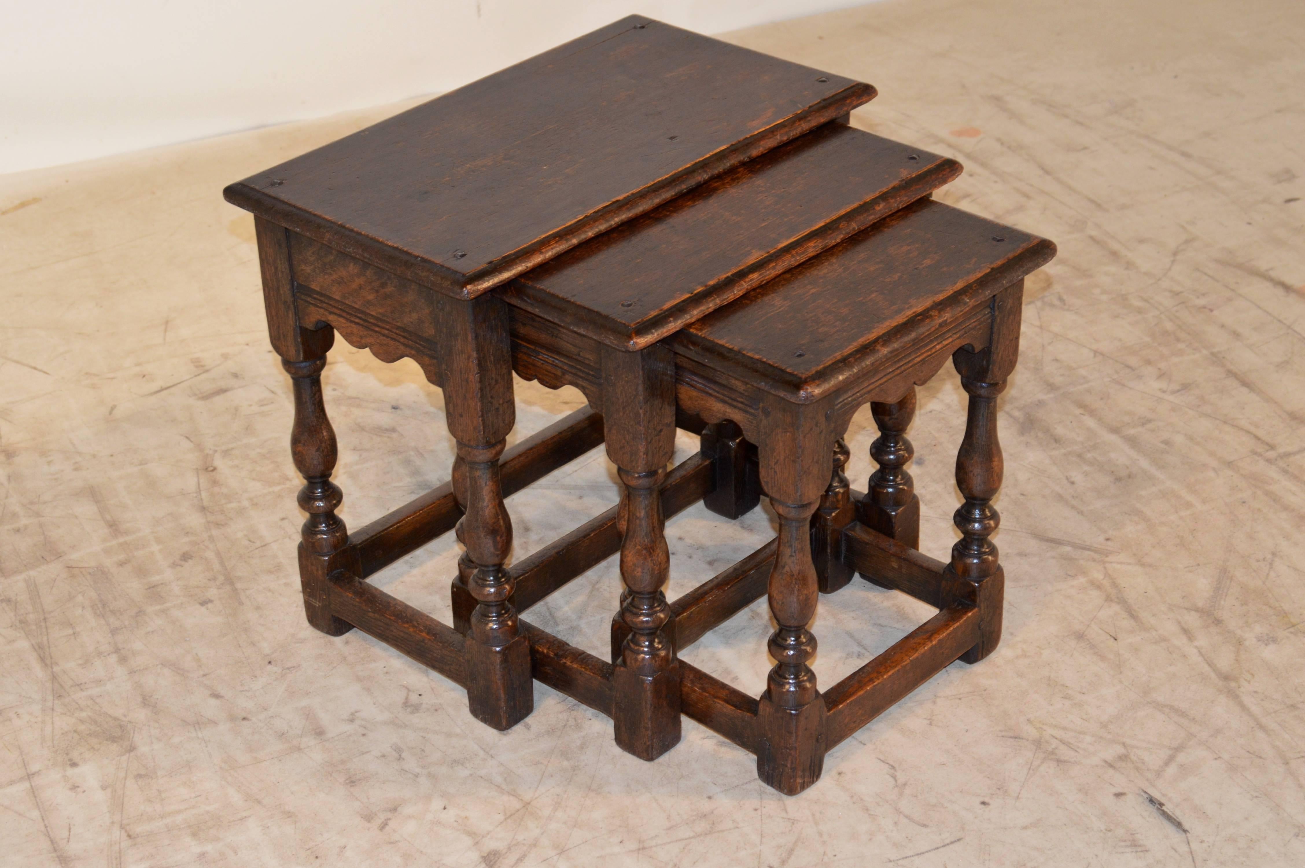 Set of three late 19th century English oak nesting tables. The tops are beveled around the edges and follow down to scalloped and routed decorated aprons. The legs are hand-turned and are joined by stretchers. Measures: Small table, 12.75