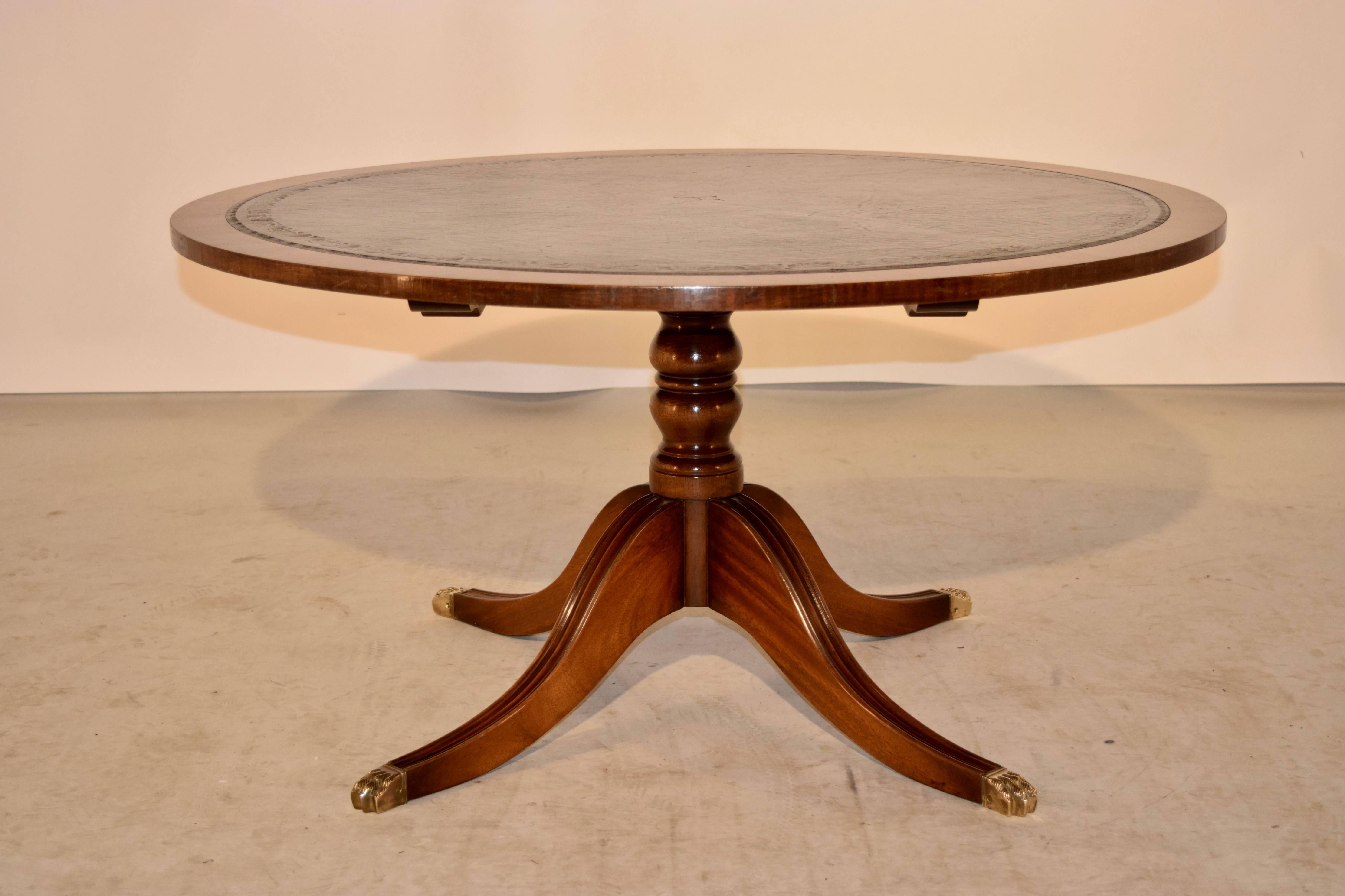 Coffee table made from Mahogany from England. The top is banded in lovely grained mahogany and the center panel is rich green leather with a gold tooled edge. The pedestal is nicely turned and ends in four legs, capped with brass paw feet, circa