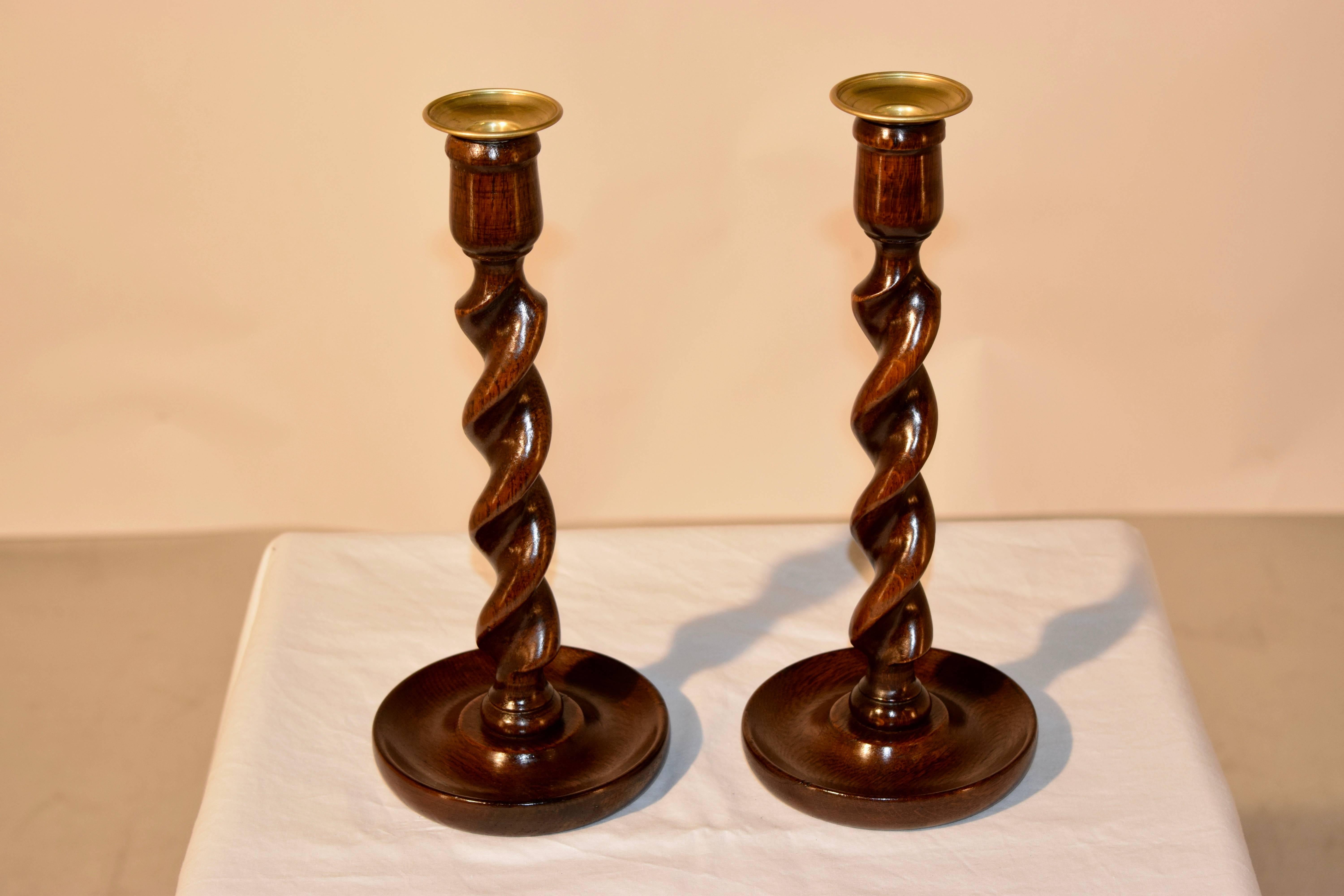 Late 19th century pair of turned oak candlesticks with hand cast brass bobeches, following down to hand-turned barley twist stems resting on hand-turned dish bases.