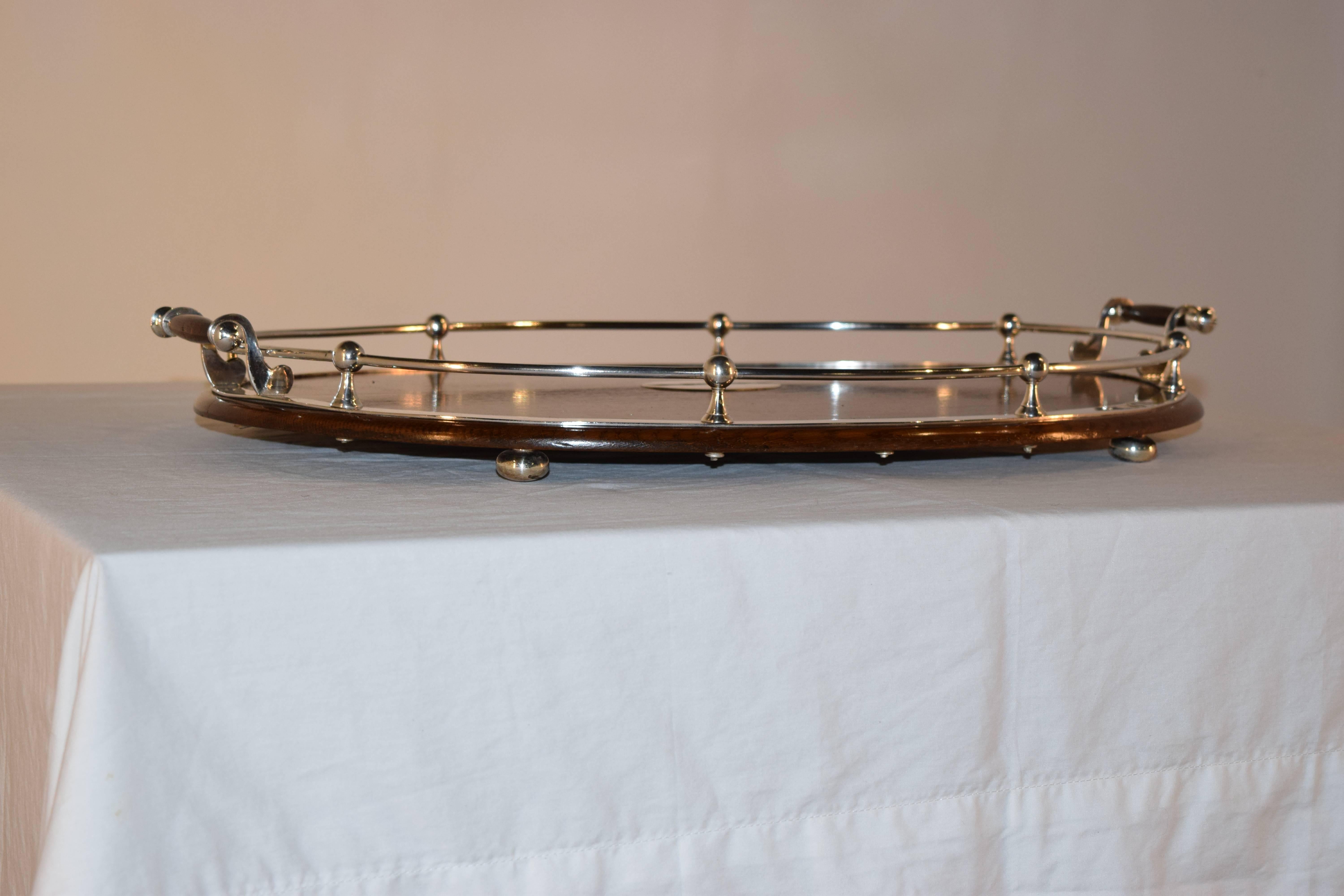 Late 19th century silver plate banded tray from England. The tray is made from oak and has a central silver plate plaque and banded around the edge, with an attached gallery as well. The tray is supported on silver plated bun feet.