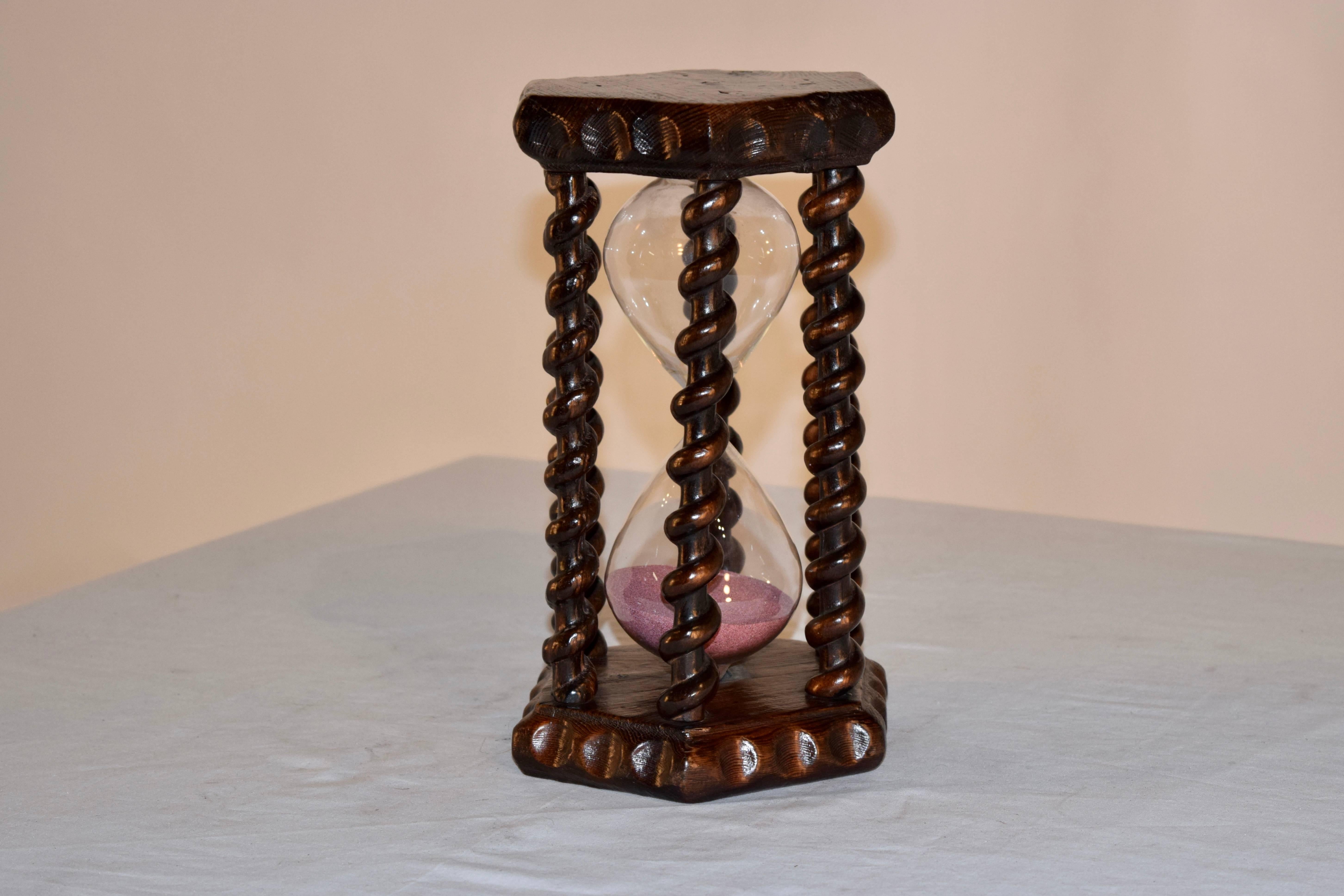 19th century English hourglass made from pine. The top and bottom have hand-carved pie crust edges and are joined together by hand-carved and turned rope twist spindles, surrounding a handblown hourglass.