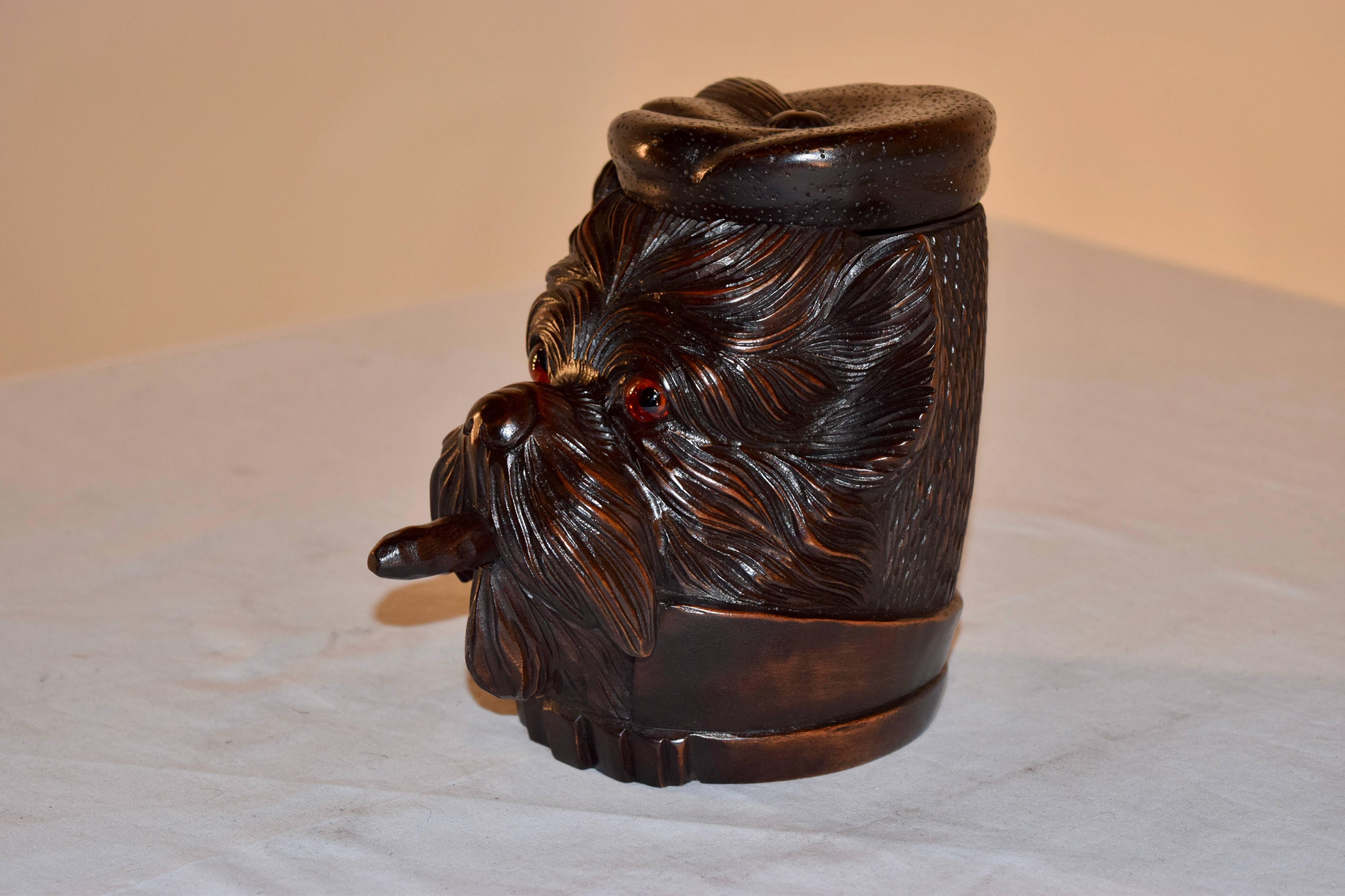 19th century black forest hand-carved humidor in the shape of a terrier. His hat lifts to reveal open storage for tobacco, and he is smoking a cigar. Original glass eyes.