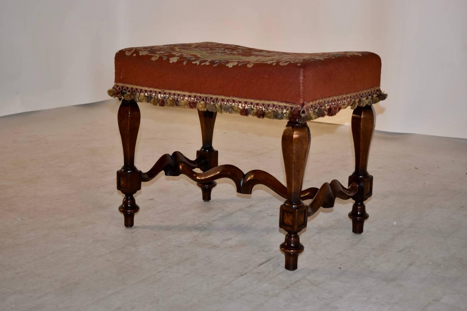 19th century French stool made from mahogany with a needlepoint upholstered seat, which is worn from age and use and has a tassel fringe trim. The legs are hand-turned and are joined by shaped stretchers. Raised on hand-turned feet.