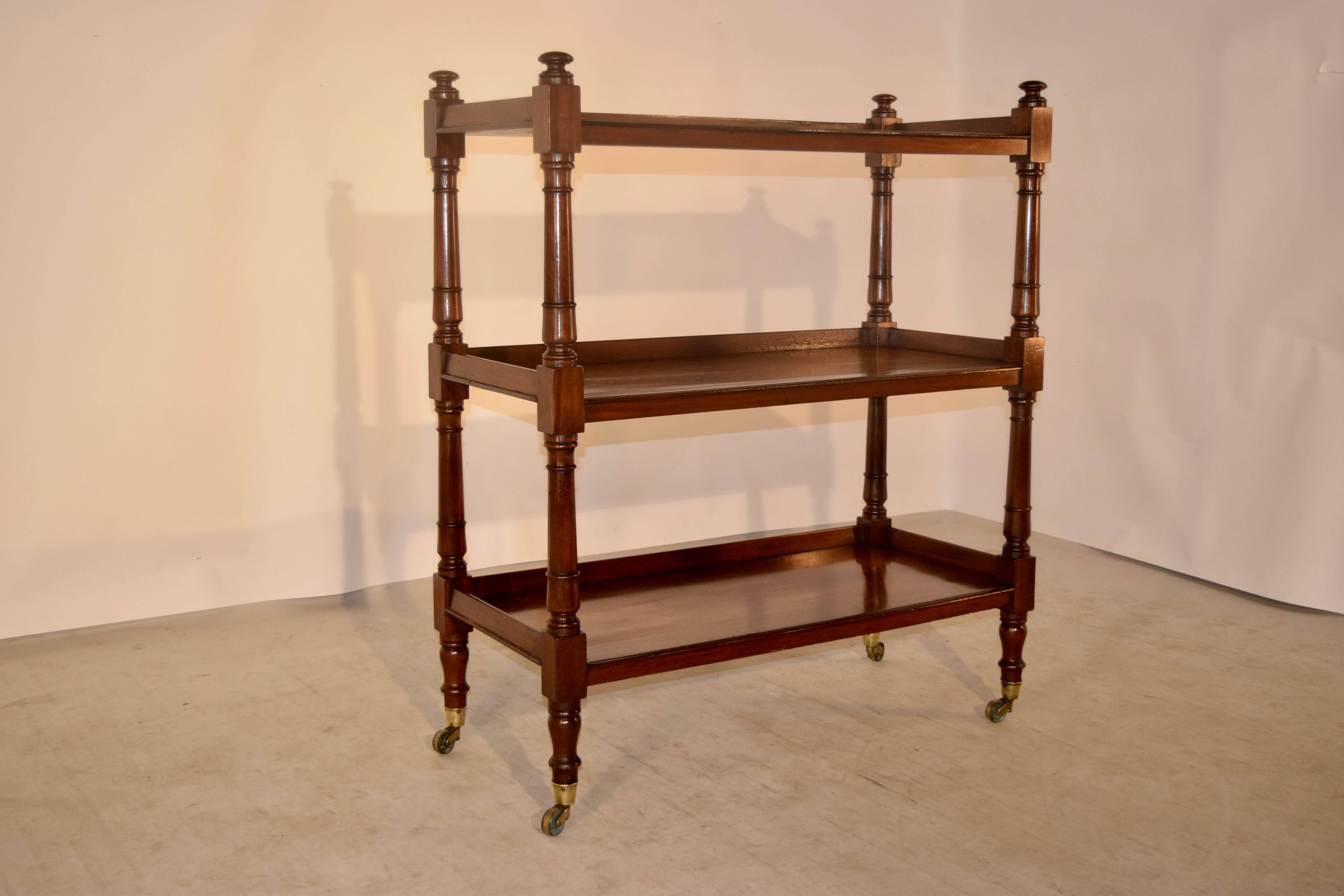 19th century English mahogany dumbwaiter with three shelves and hand turned legs and shelf supports. Raised on brass casters. The shelves have normal staining and signs of wear for age and use.