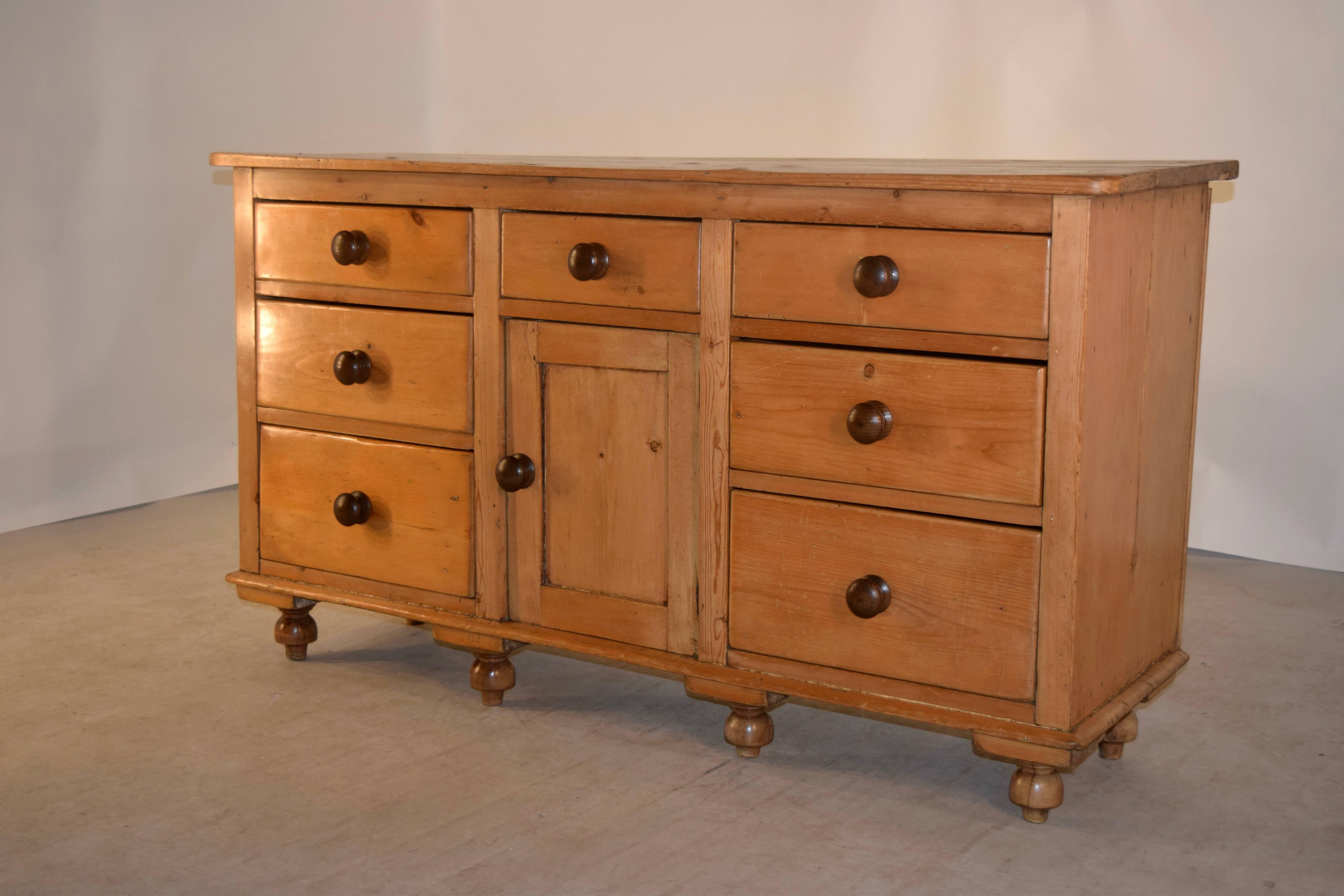 19th century pine dresser base from England. The top is made up of planks, and follow down to simple sides and two banks of three drawers each flanking a central drawer and lower door, which opens to reveal storage. Raised on hand turned feet.