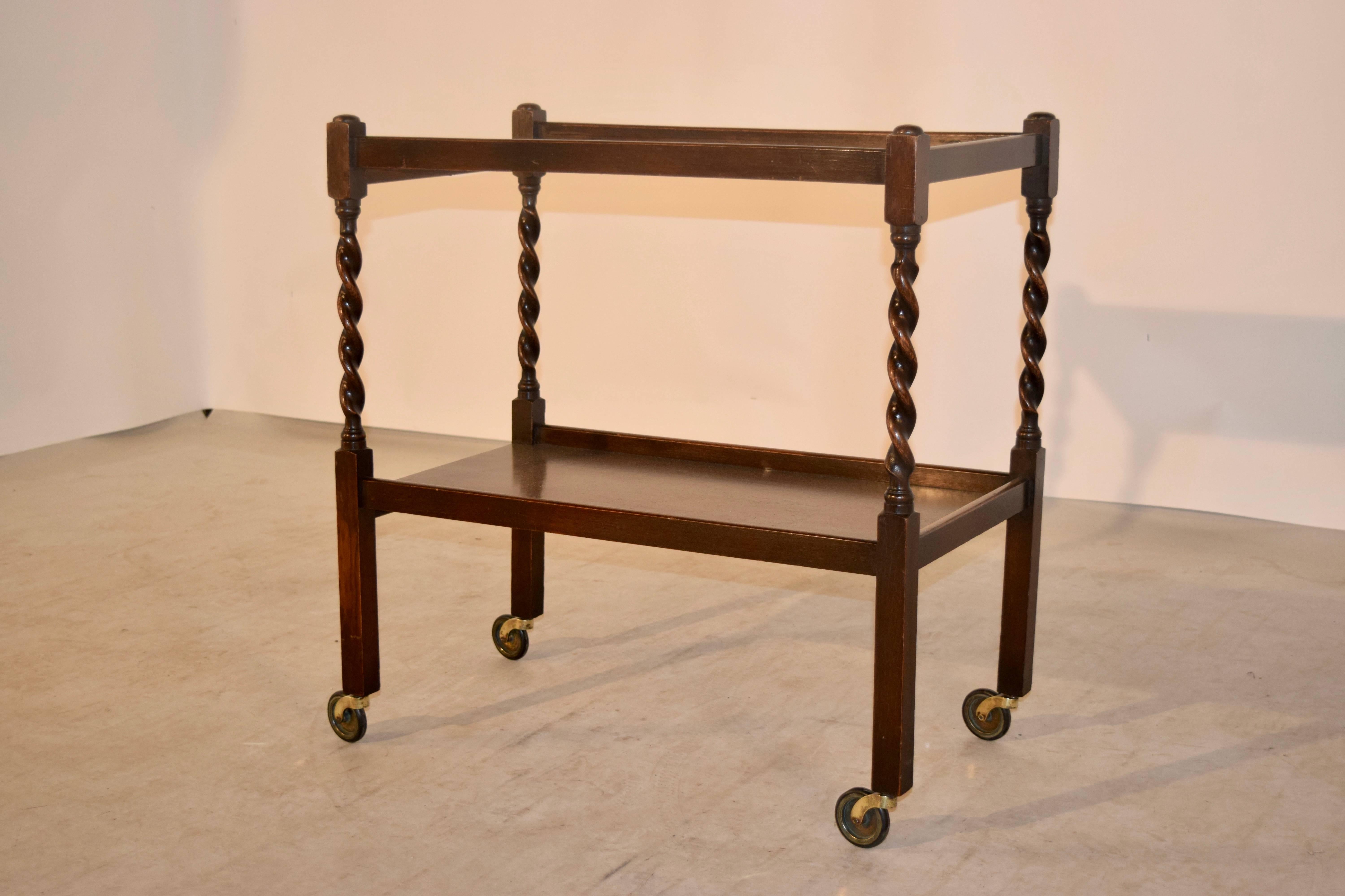 English oak drink cart, circa 1900. This cart has two shelves, separated by hand turned barley twist shelf supports, and straight legs at the bottom for contrast. Raised on casters.