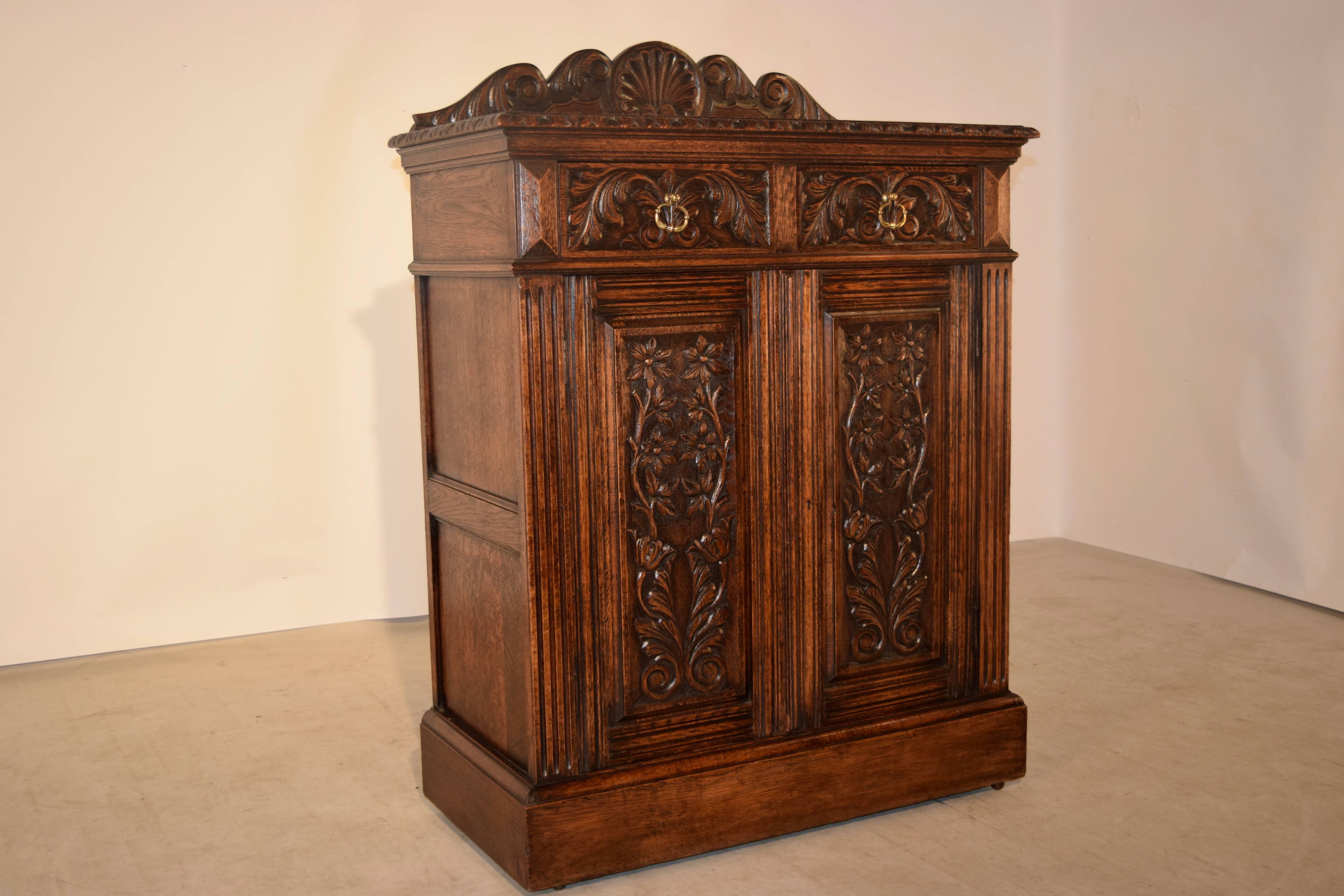 19th century English cupboard made from oak. The top is decorated with a hand-carved backsplash, and a beveled and hand-carved edge, following down to two drawers over two doors, all with hand-carved floral decoration. The doors open to reveal