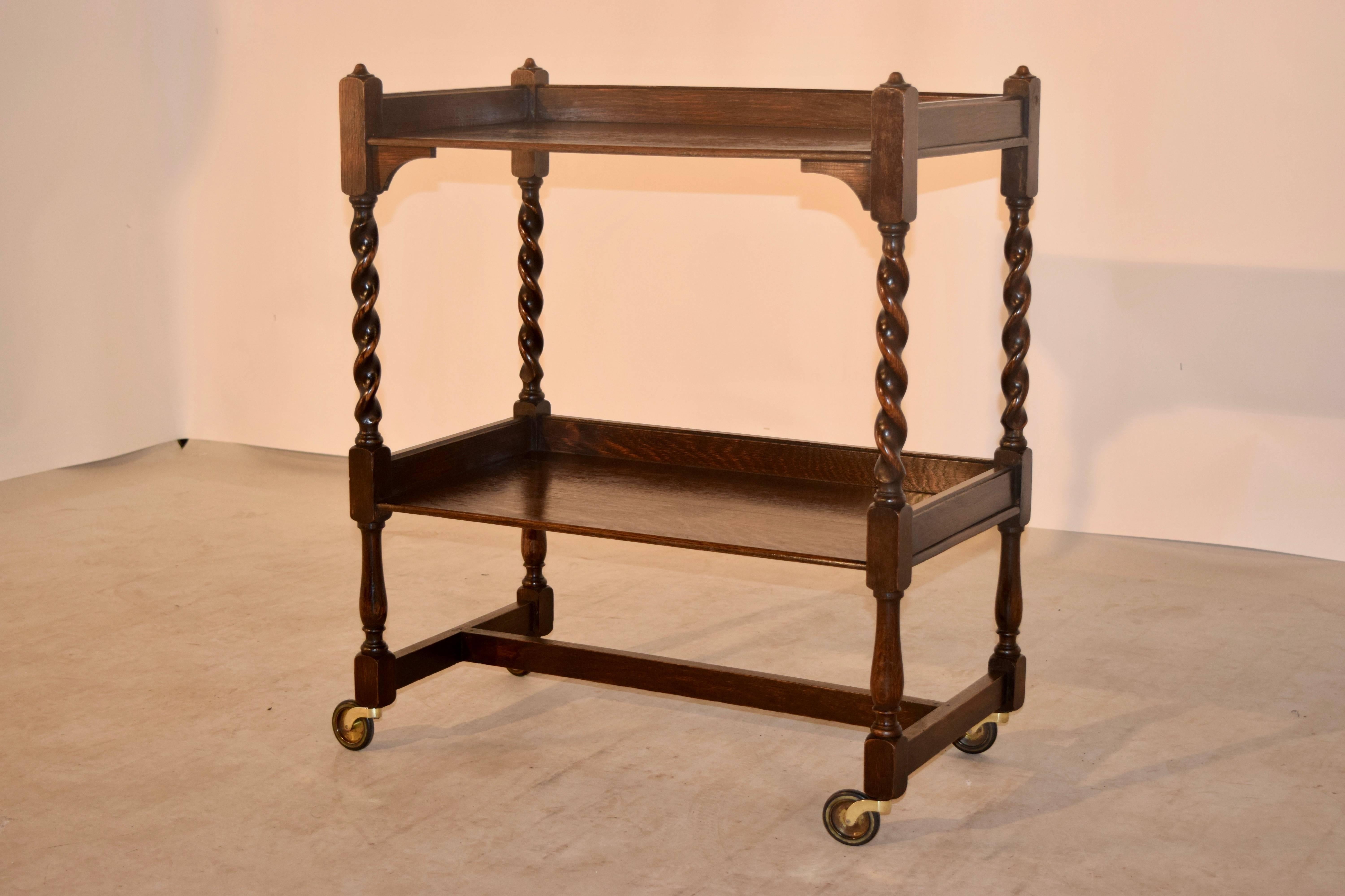 English oak drink cart, circa 1900. This piece has two shelves, separated by hand turned barley twist shelf supports and turned legs at the bottom for contrast, joined by simple stretchers. Raised on casters.